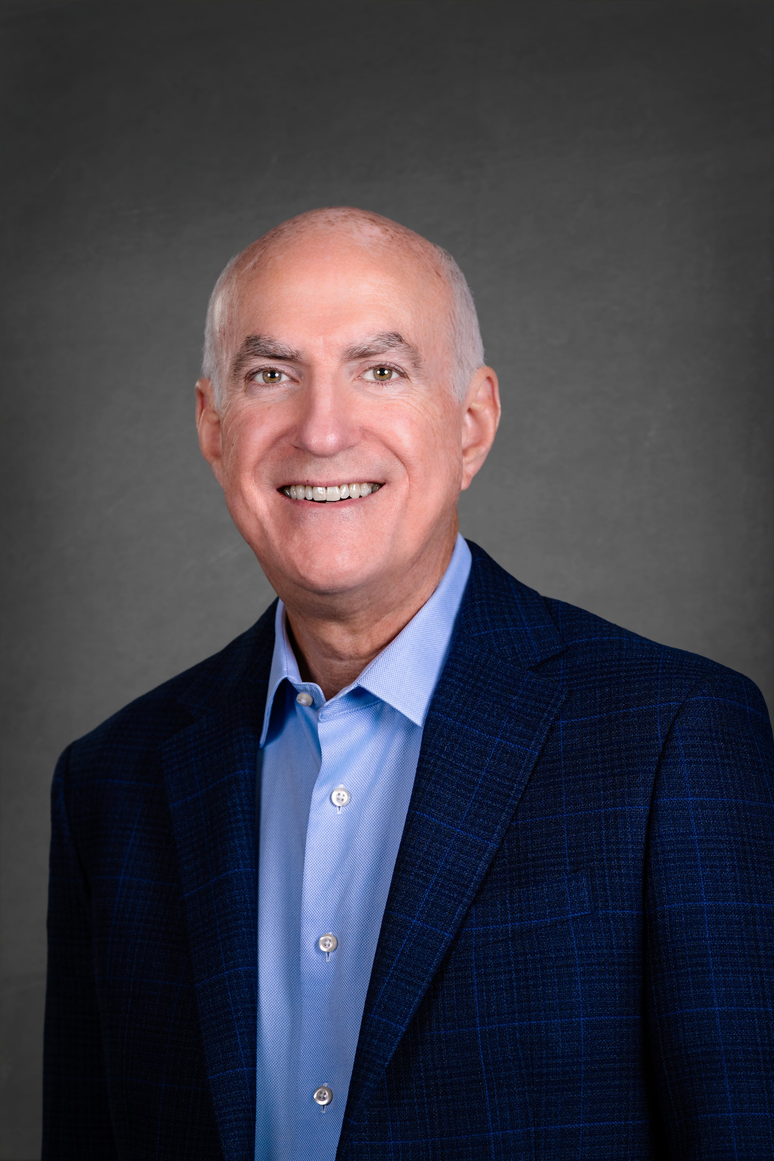 Professional headshot of Phil Zaheretti, a smiling executive/leader/speaker in a blue suit and collared shirt.