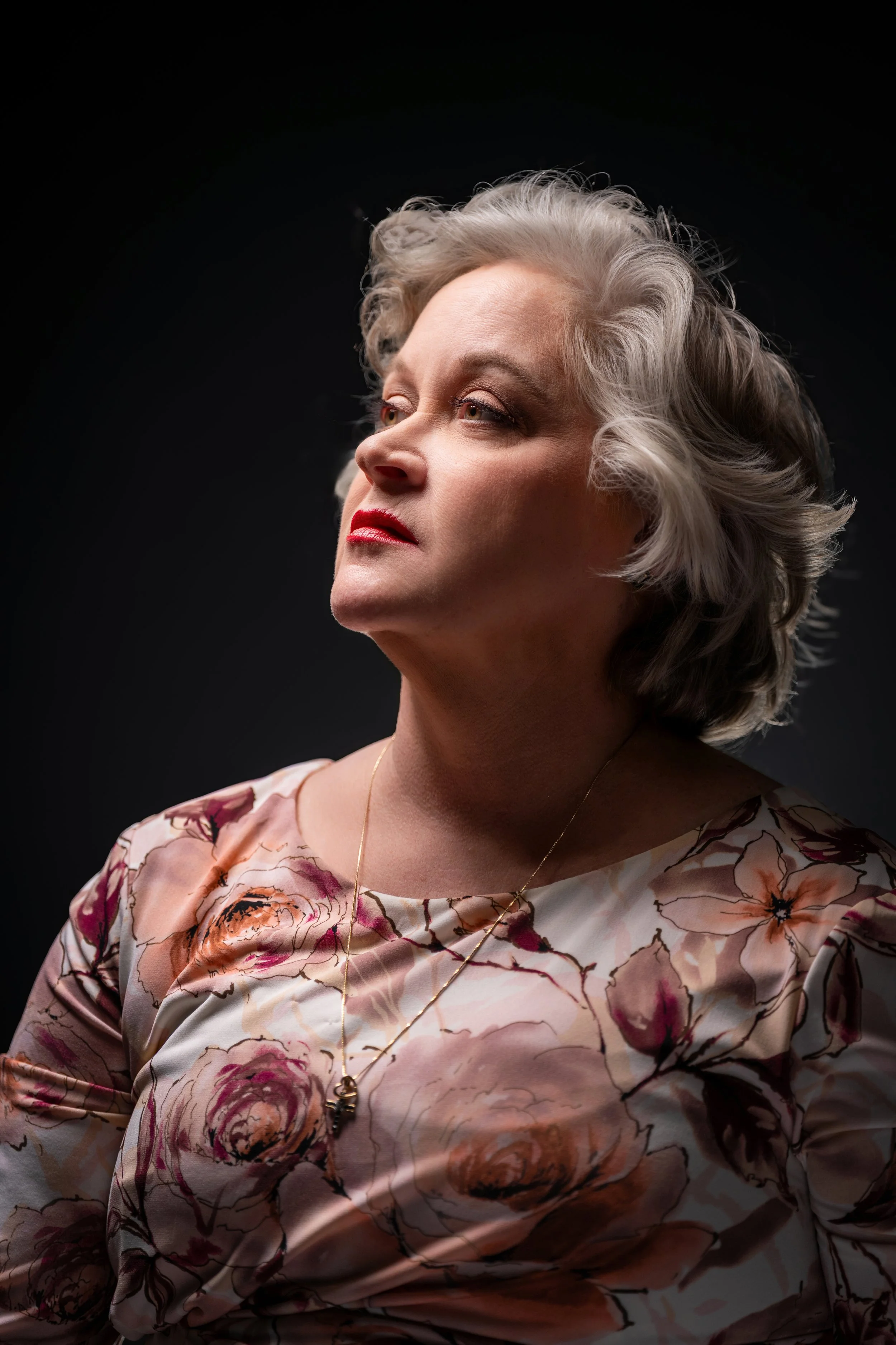 ortrait of a woman with white hair, looking up and to the left, wearing a floral patterned top.