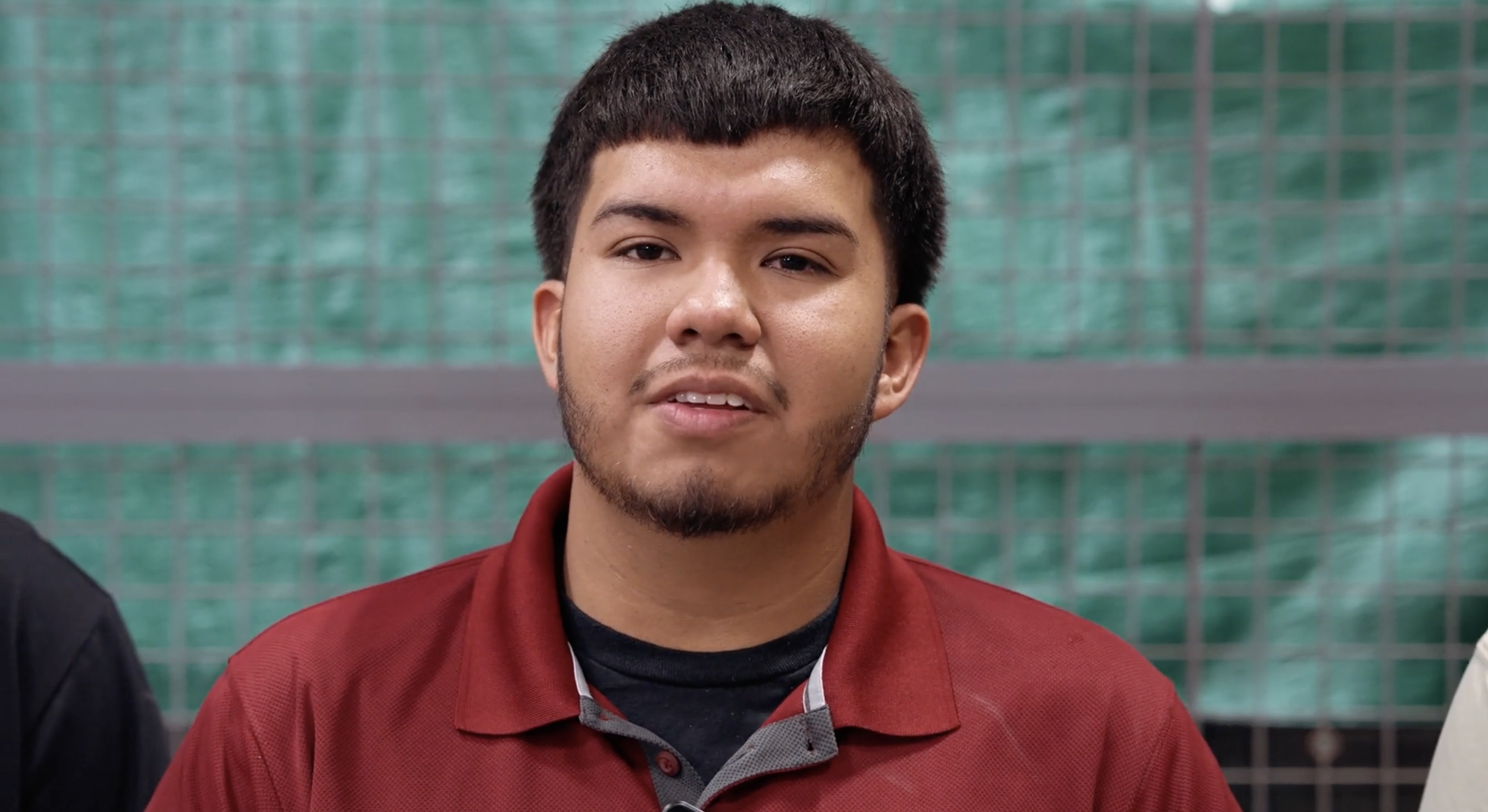 A person wearing a maroon polo shirt looking at the camera with a green background.