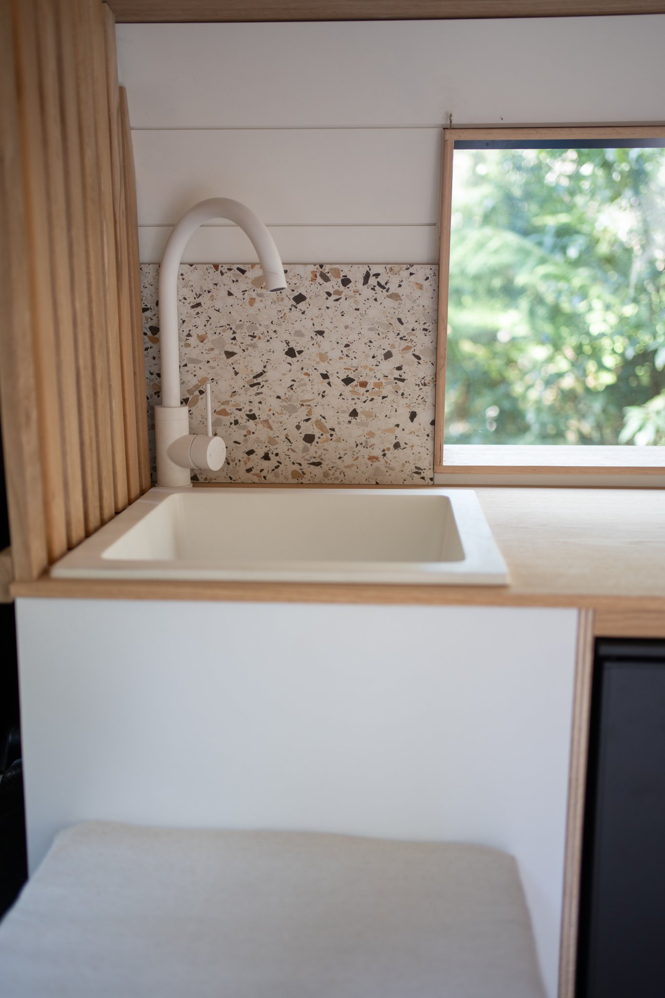 Compact kitchen with white sink, modern faucet, terrazzo backsplash, and a window with natural view.