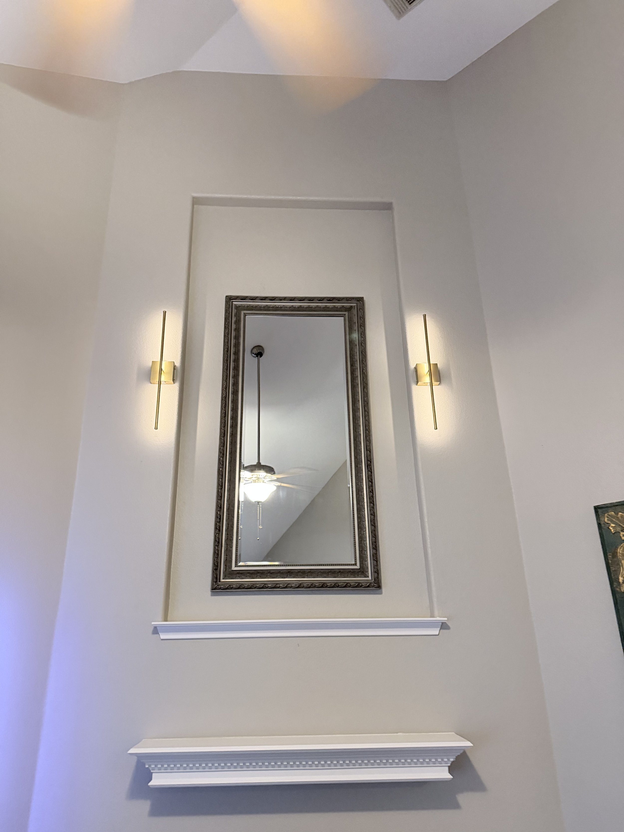 Wall sconces installed with centered mirror and clean trim detail for balanced interior lighting.
