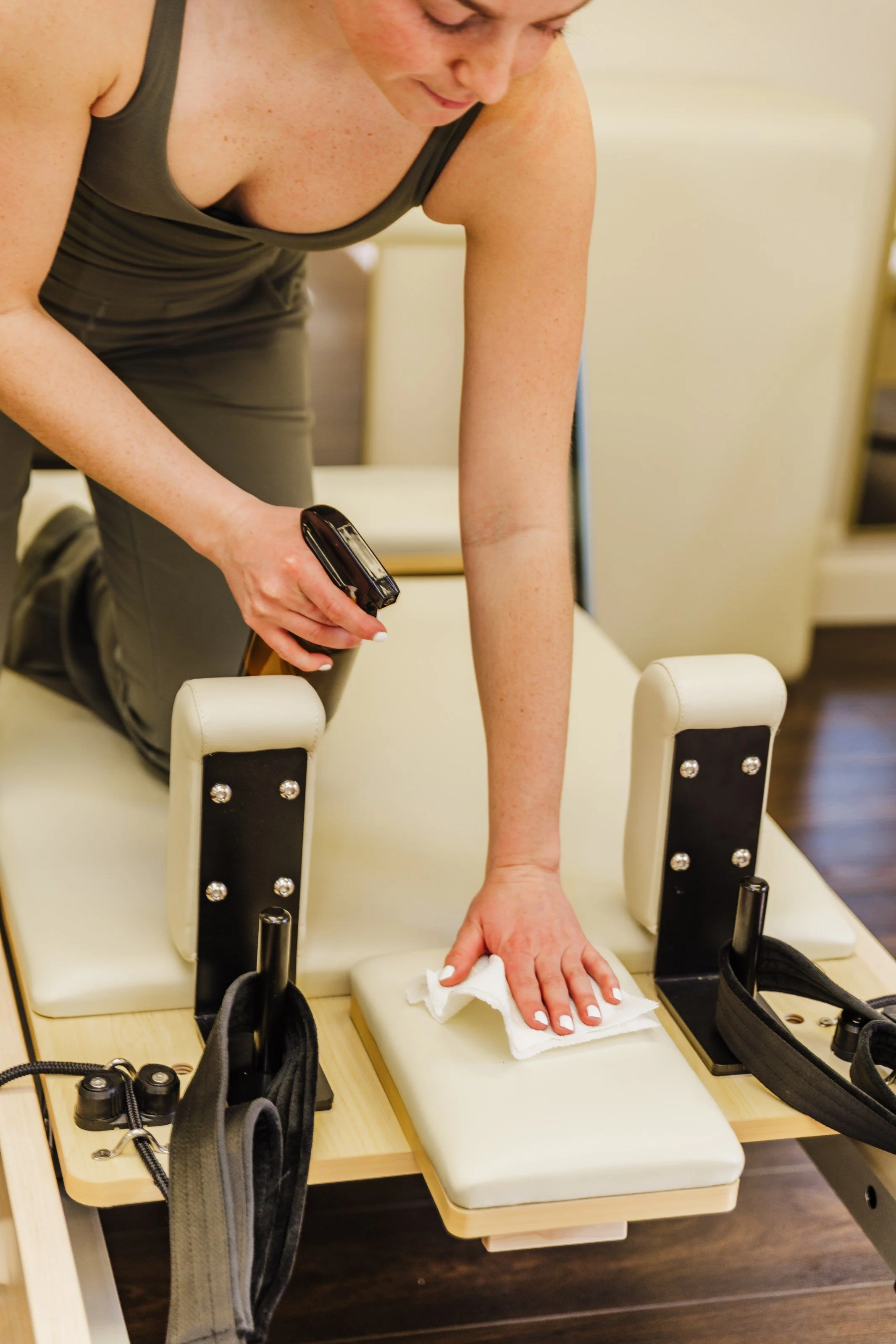A woman performing a physical therapy exercise on a specialized bed, wiping the surface with a cloth while holding an infrared thermometer.