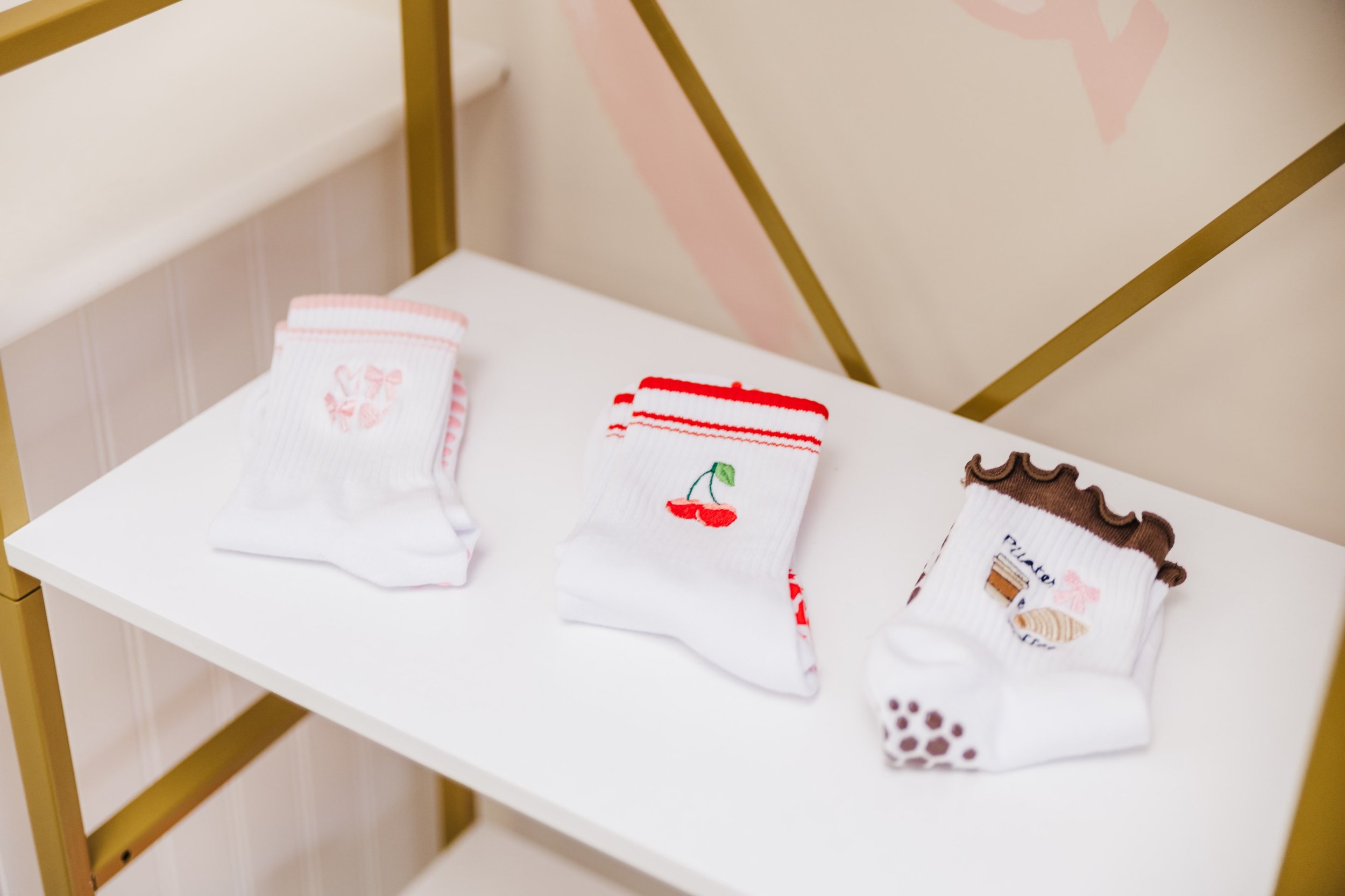 Three pairs of white socks with colorful embroidered designs, decorated with pink, red, and brown patterns, displayed on a white table.