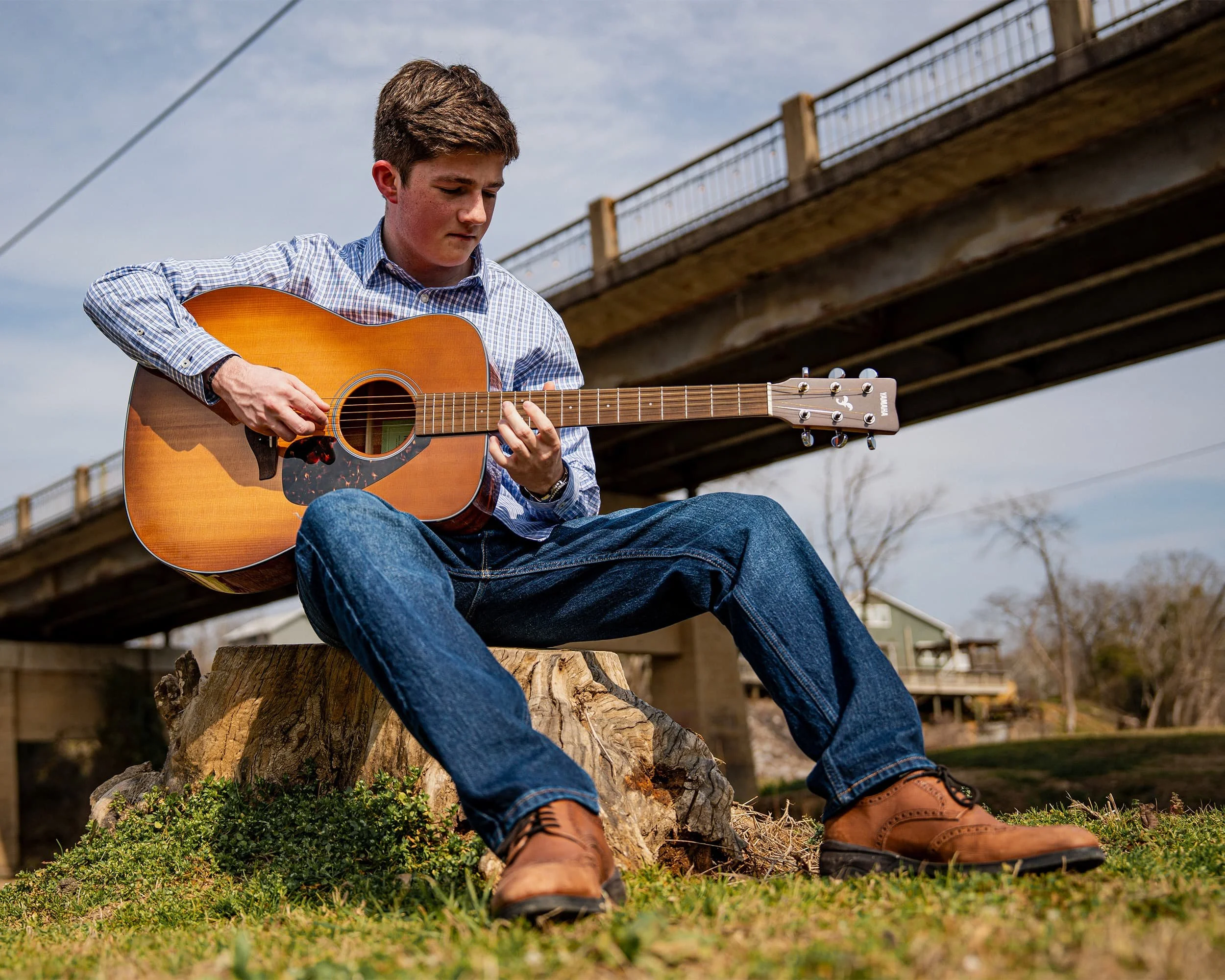 portrait of a guy playing guitar under a bridge