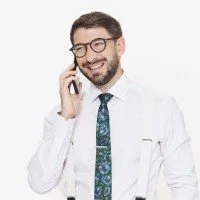 Smiling man wearing glasses, white shirt, tie, and suspenders talking on the phone