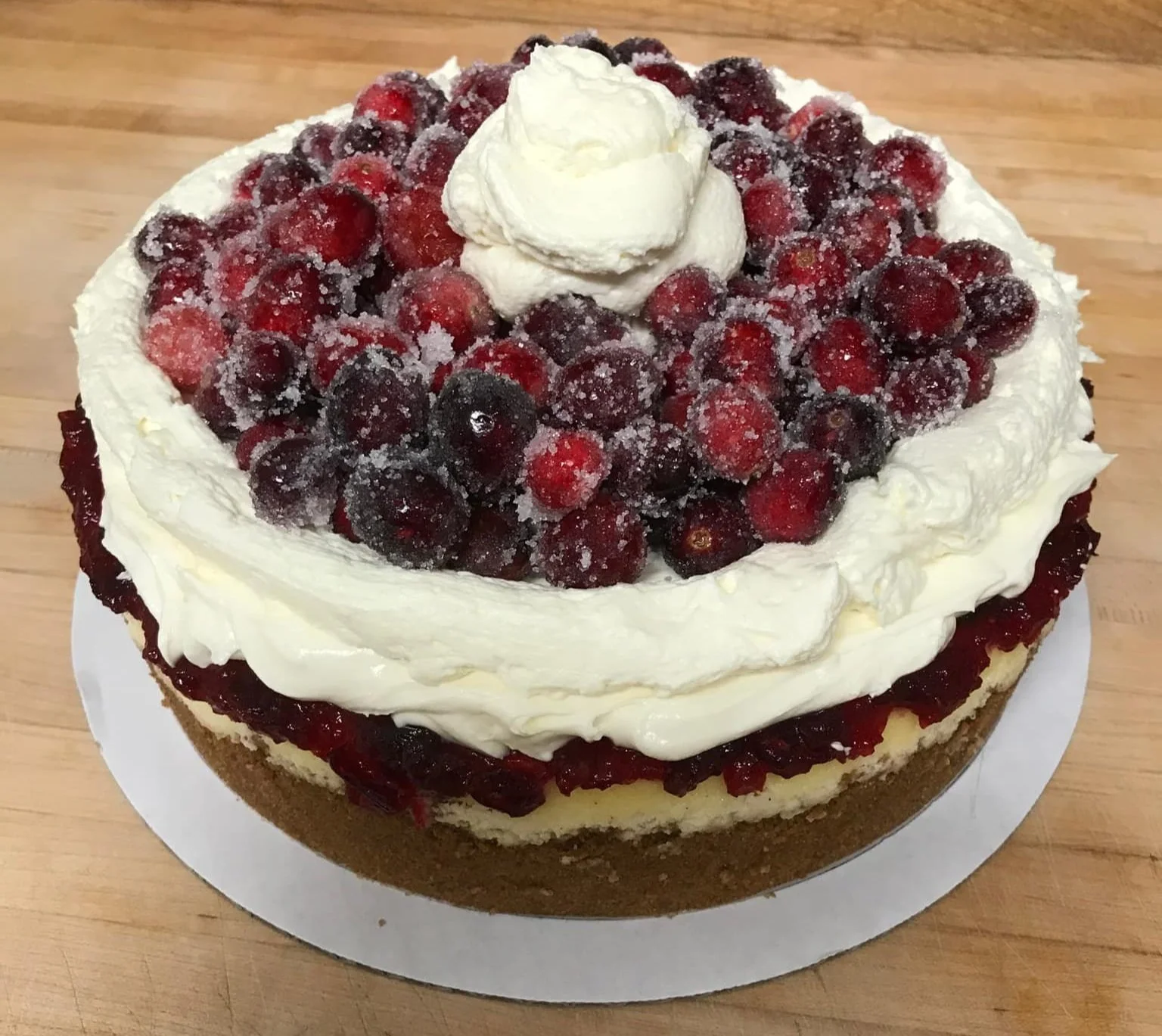 A layered berry cheesecake topped with a mix of fresh berries, whipped cream, and a dollop of whipped cream in the center.