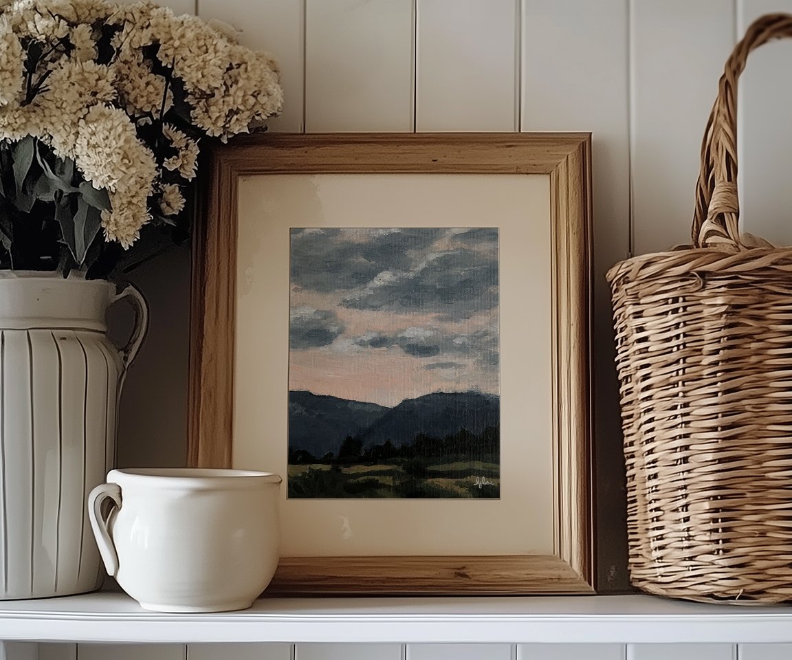 pantry shelf with basket, flowers and framed painting of pink sky with blue clouds over blue mountains and green field