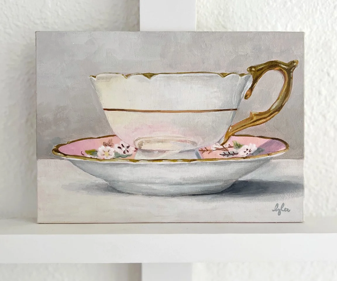 painting of white teacup and saucer with gold handle against white wall