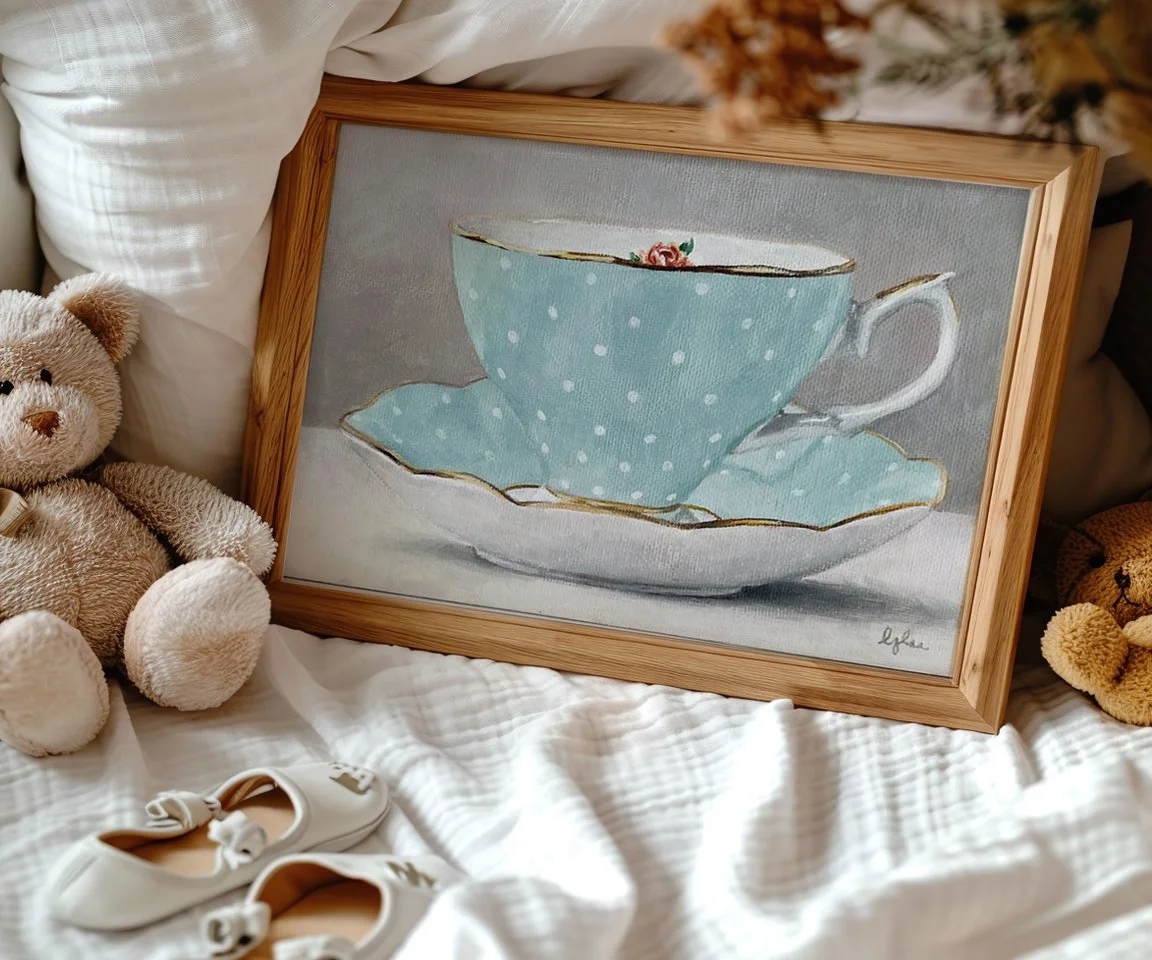 framed painting of light blue teacup and saucer with white polka dots and rose inside rim of cup on bed with baby items