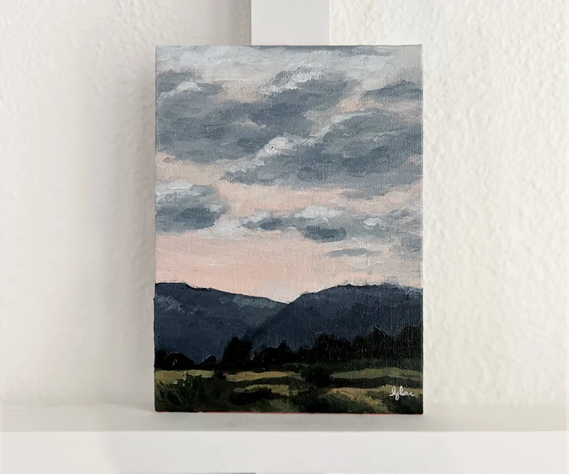 painting of pink sky with blue clouds over blue mountains and green field