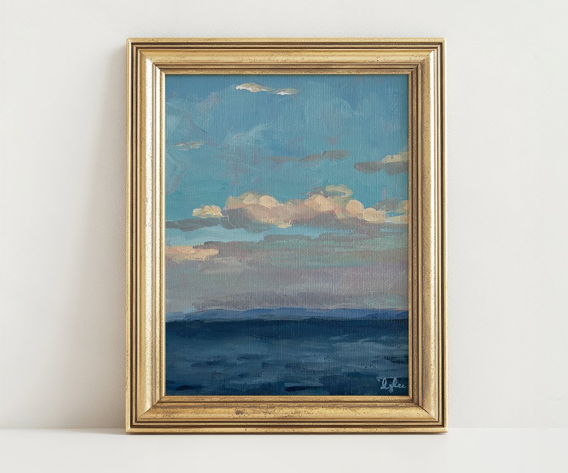 gold framed painting of clouds in blue sky over ocean against white wall