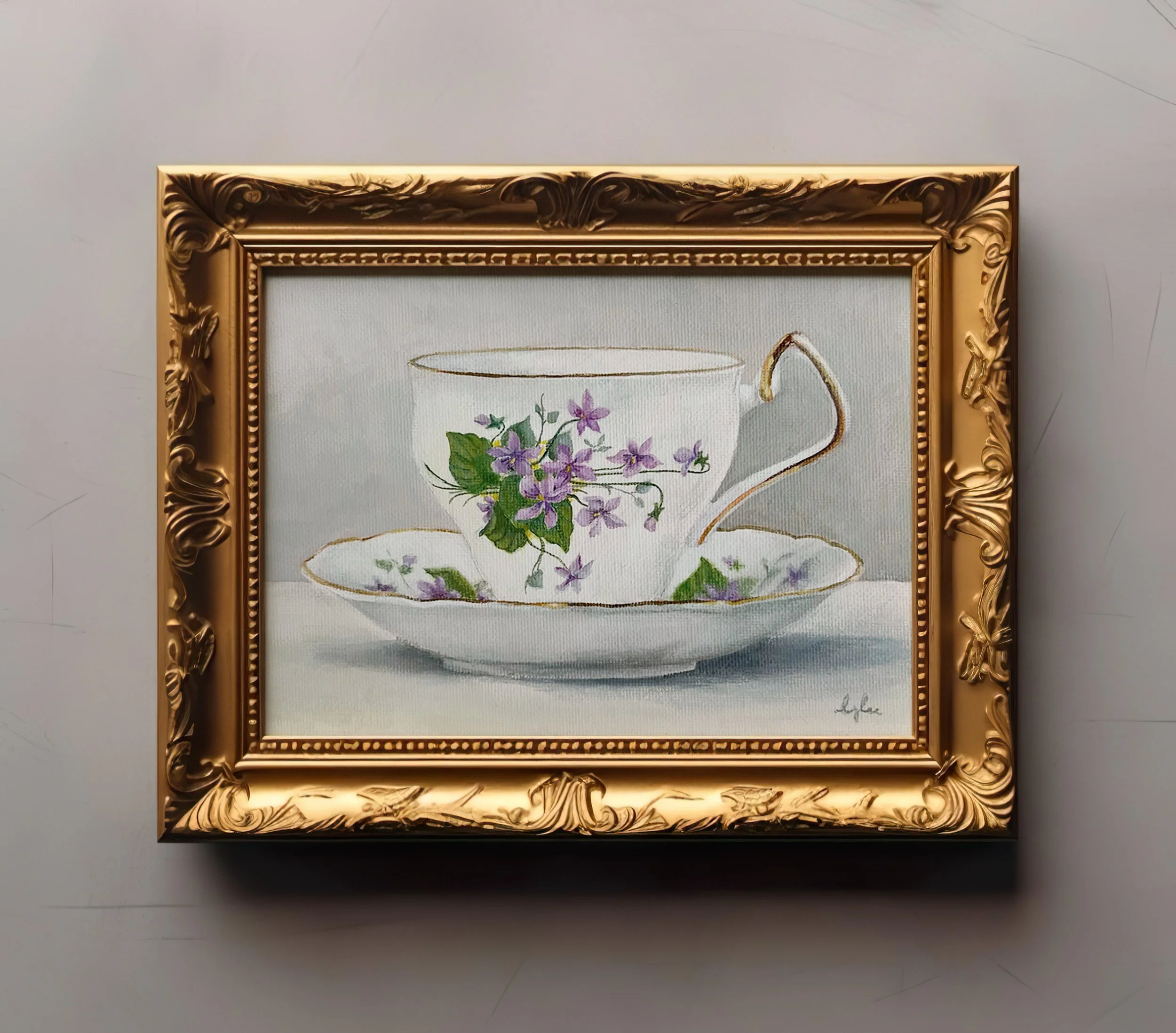 gold framed painting of teacup and saucer with bouquet of violets against wall