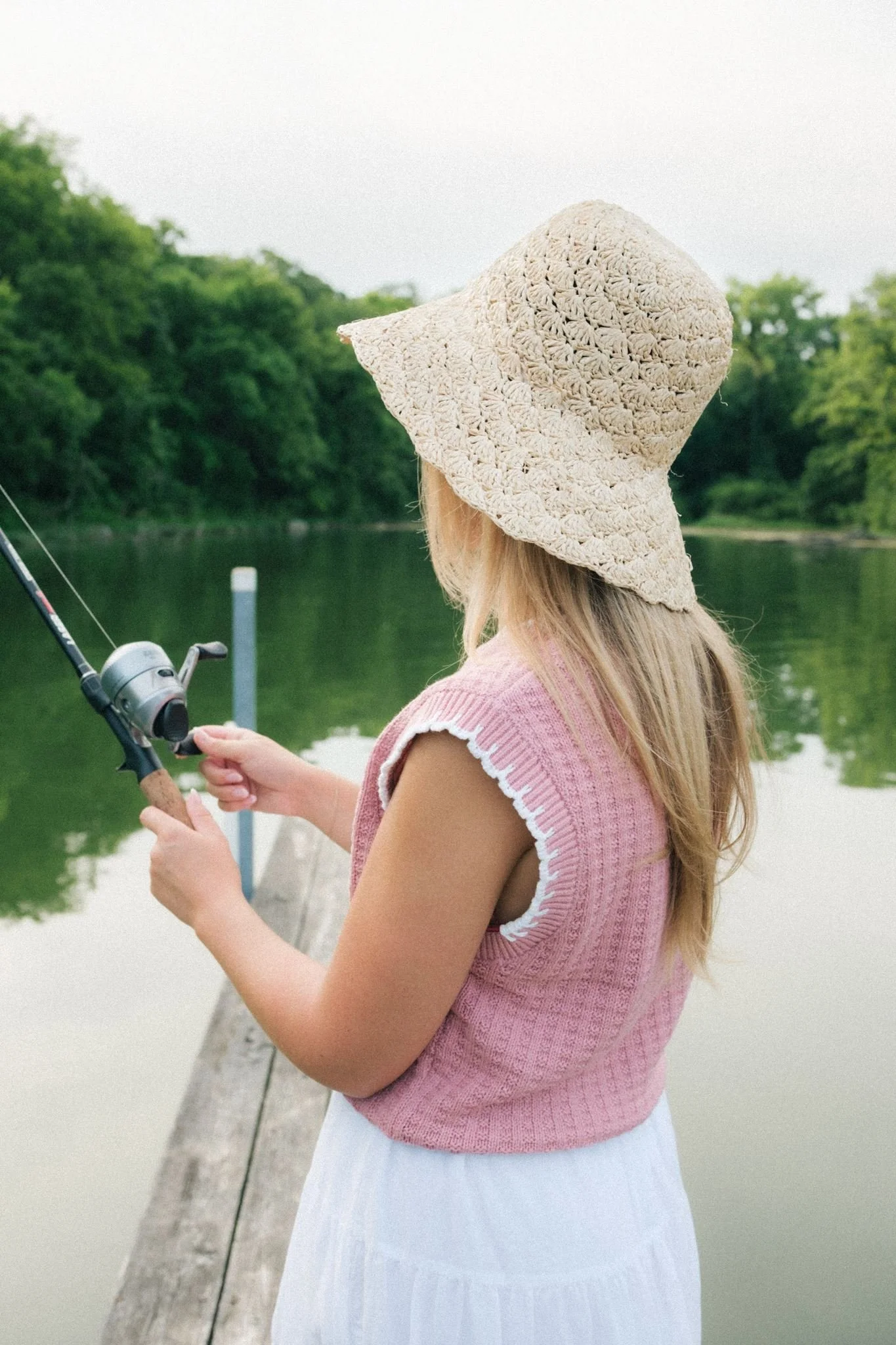 A woman fishing while wearing a straw hat.