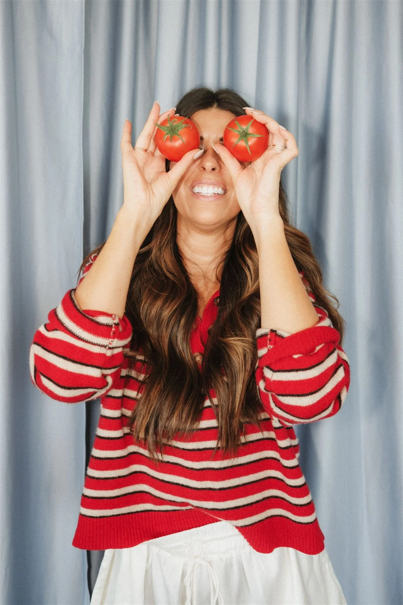  A business owner holding two tomatoes in front of her eyes, laughing.  