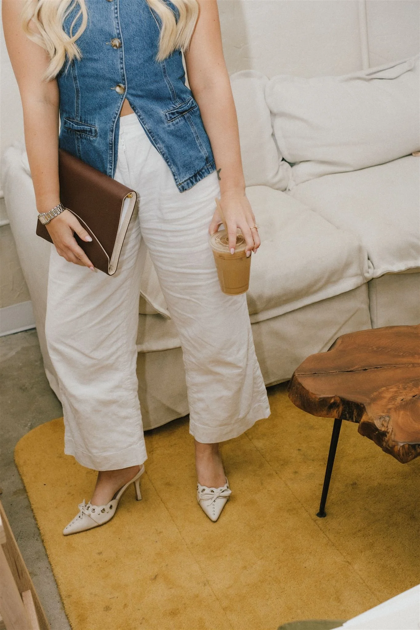  A woman holding a notebook and coffee while wearing a denim vest and white plants.  