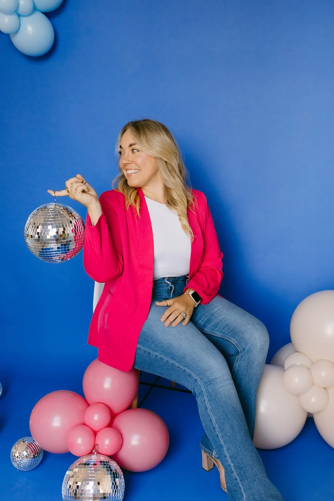  A woman sitting in a chair surrounded by balloons and disco balls for her brand photoshoot in Kansas City.  