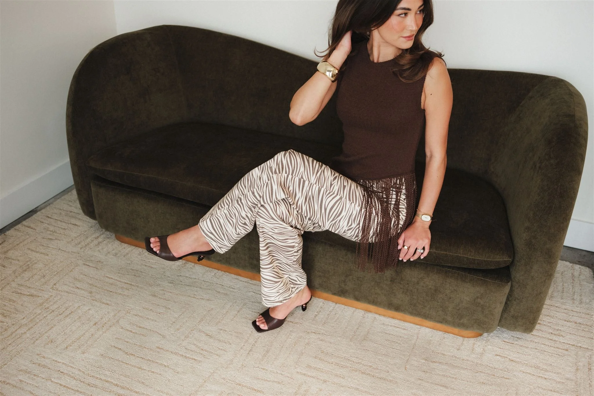 A woman sitting on a couch, adjusting her hair for her brand photoshoot.