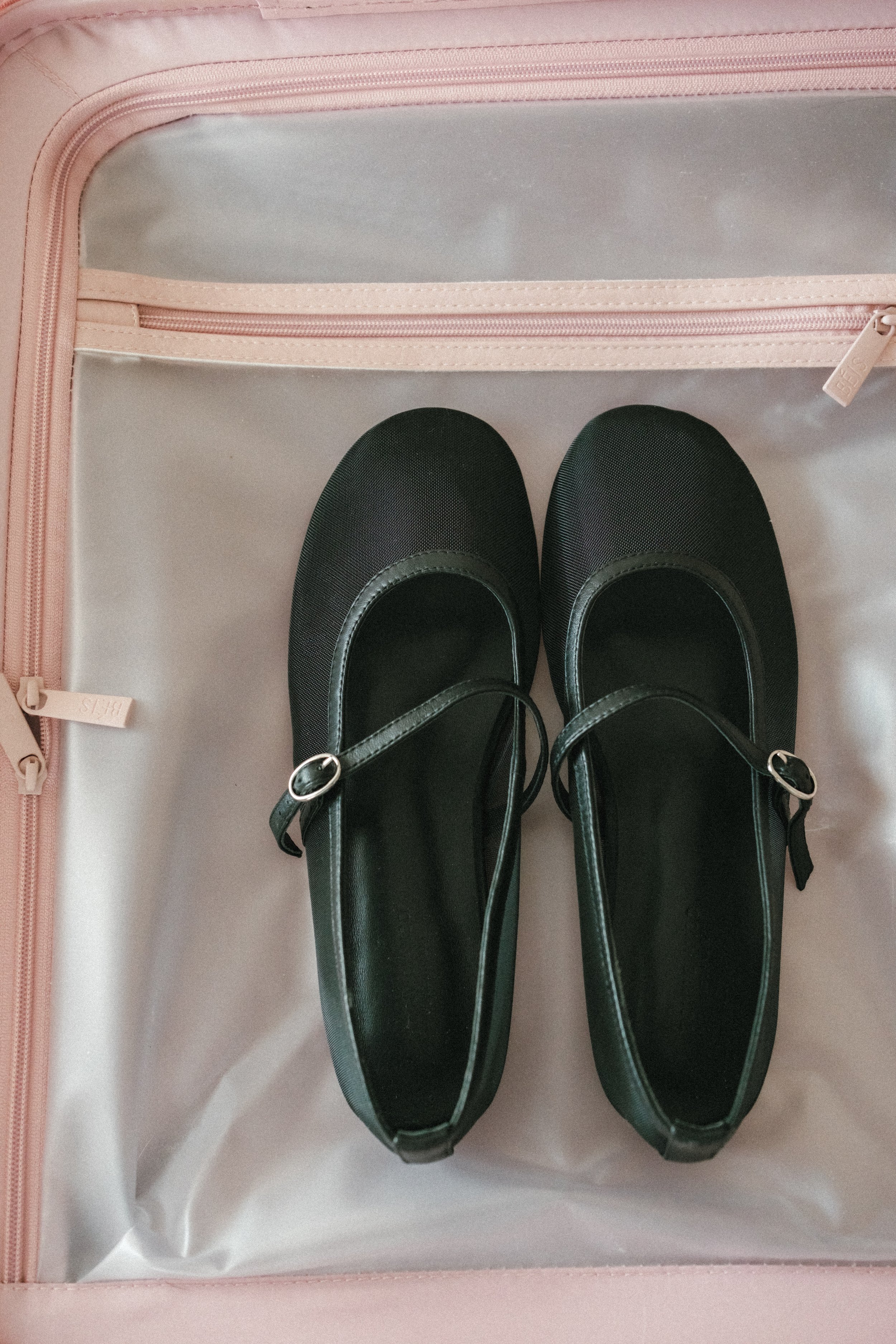 Pair of black Mary Jane shoes inside a pink suitcase.