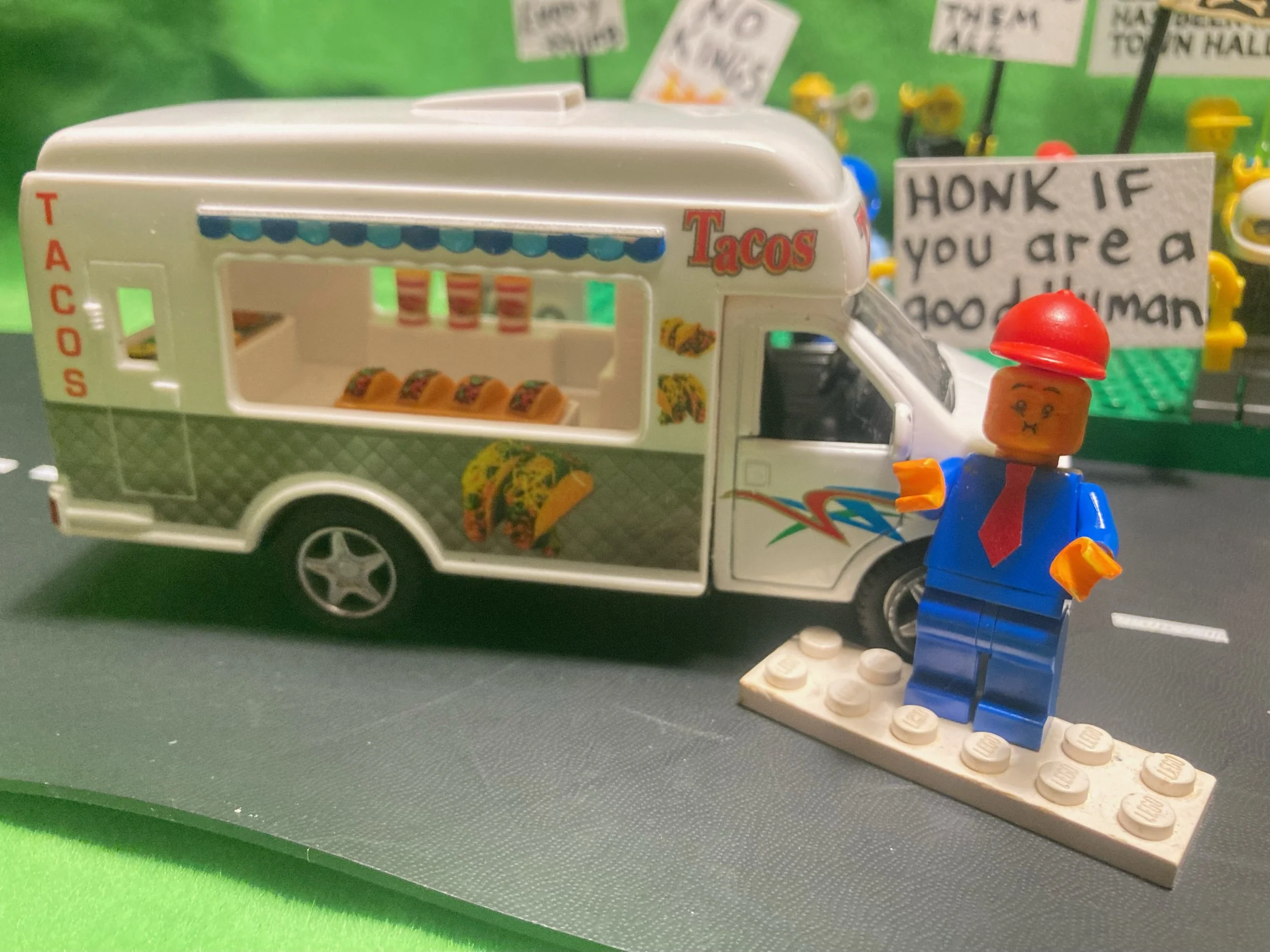 LEGO toy food truck with tacos and a LEGO minifigure in a red cap standing in front.