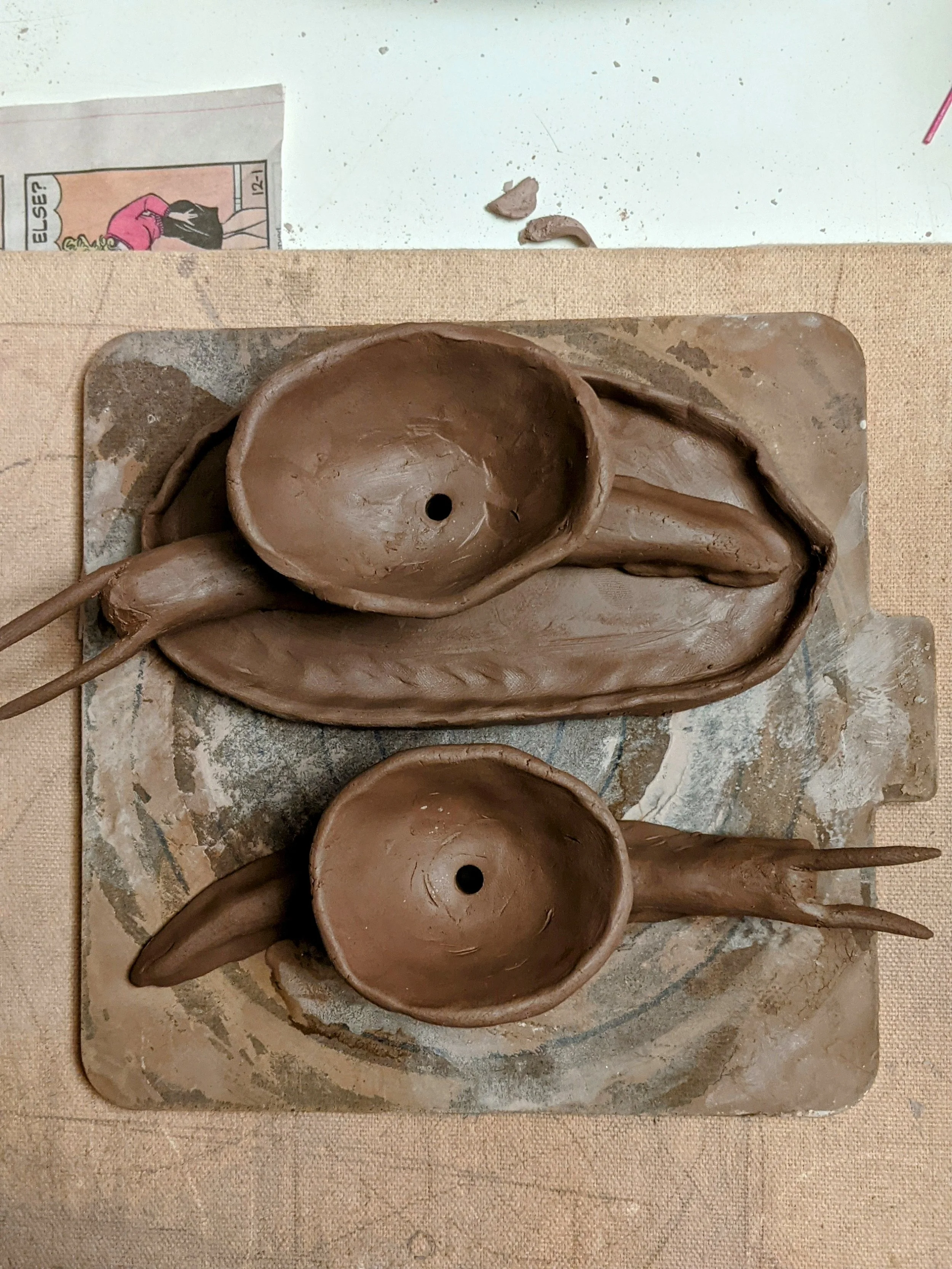 Clay planters for succulents sculpted to look like snails with bowls for shells, laying on a ceramic bat, with a beige table underneath.