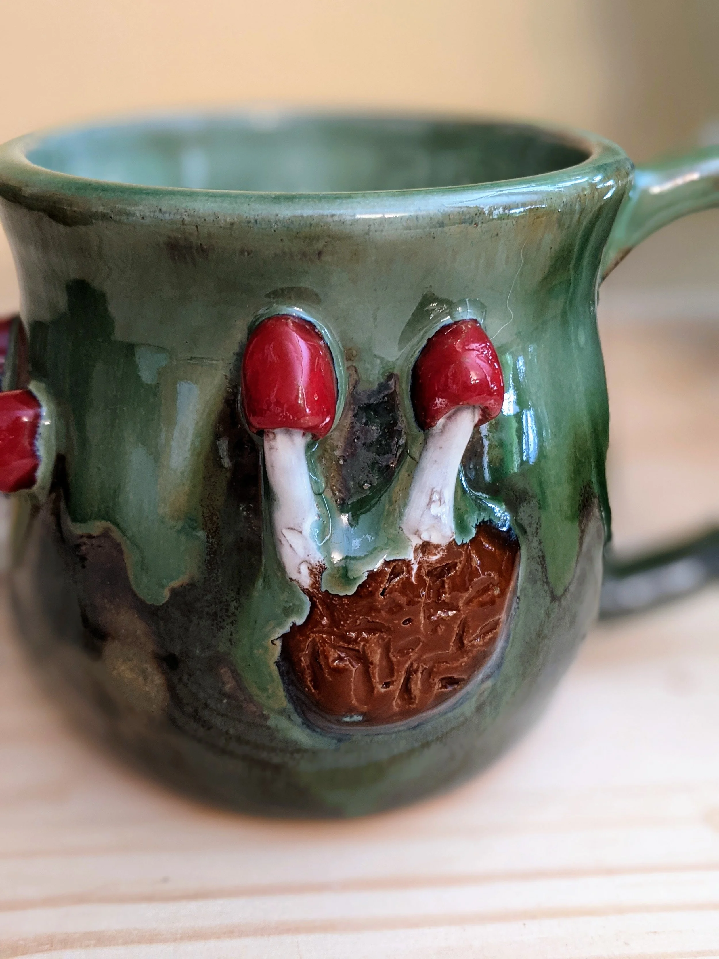 Close-up of a ceramic mug with a skull face design, featuring red eyes and a brown nose and mouth area, on a light-colored wooden surface.