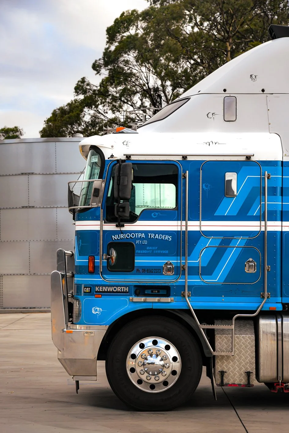 Close-up view of a Nuriootpa Traders Kenworth truck, parked outside with trees in the background.