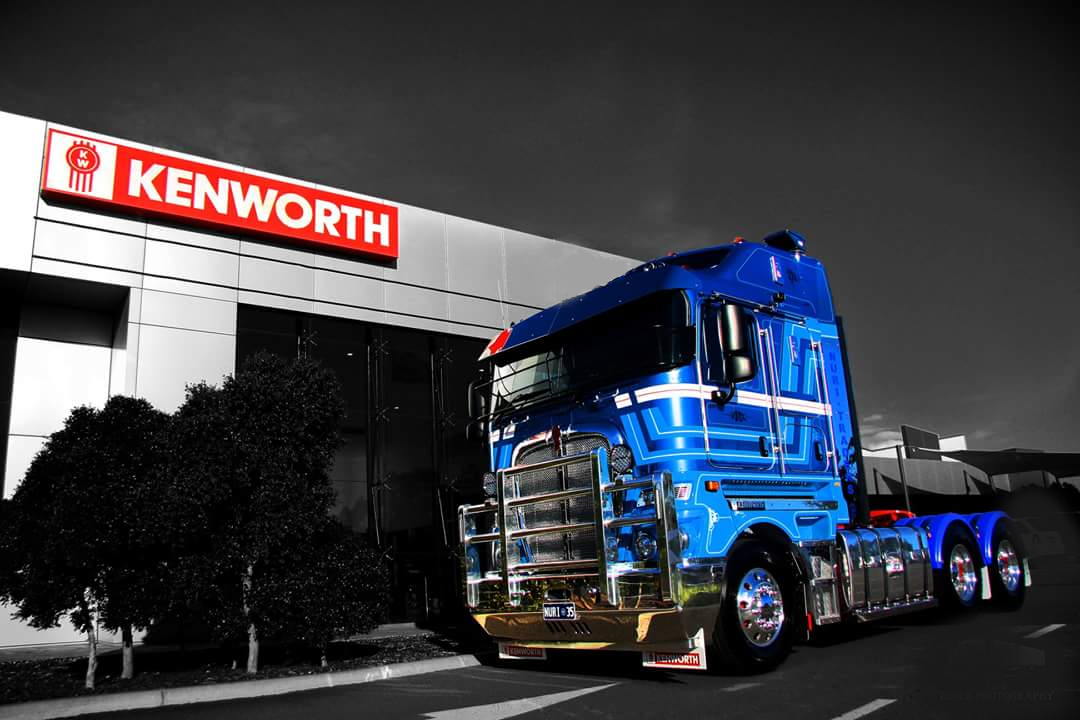 Nuriootpa Traders semi-truck parked outside the Kenworth building with trees nearby, with a cloudy sky in the background.