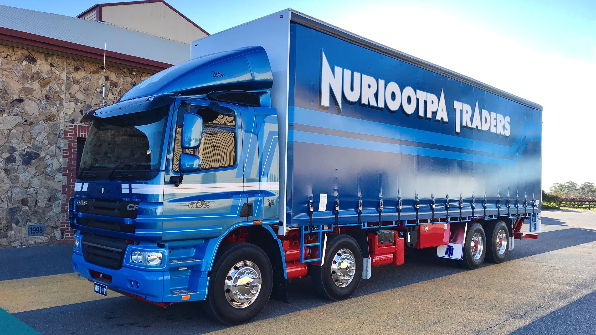 Nuriootpa Traders truck with white and red stripes parked in front of a stone building with a red trim. 
