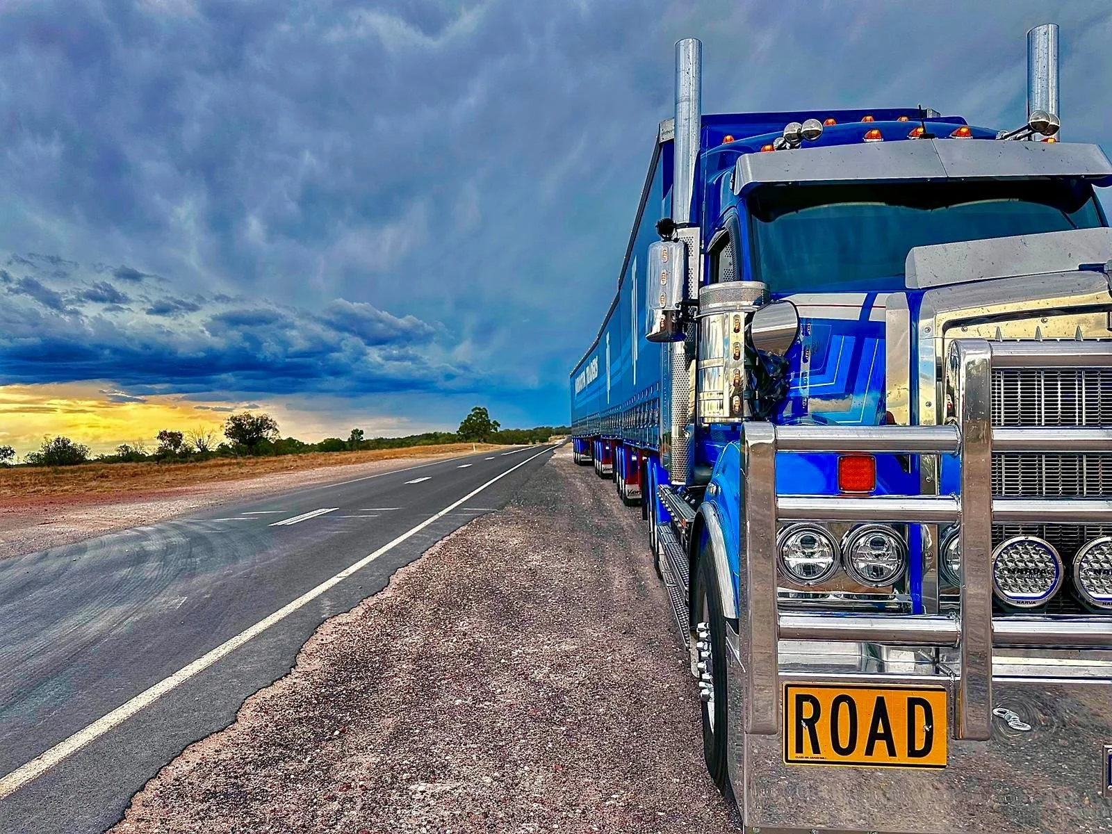 Nuriootpa Traders truck parked on the side of a two-lane road at sunset, with a yellow 'Road Train' sign on the front bumper.