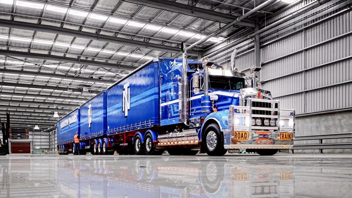 A large Nuriootpa Traders semi-truck with a matching trailer parked inside a spacious industrial warehouse.