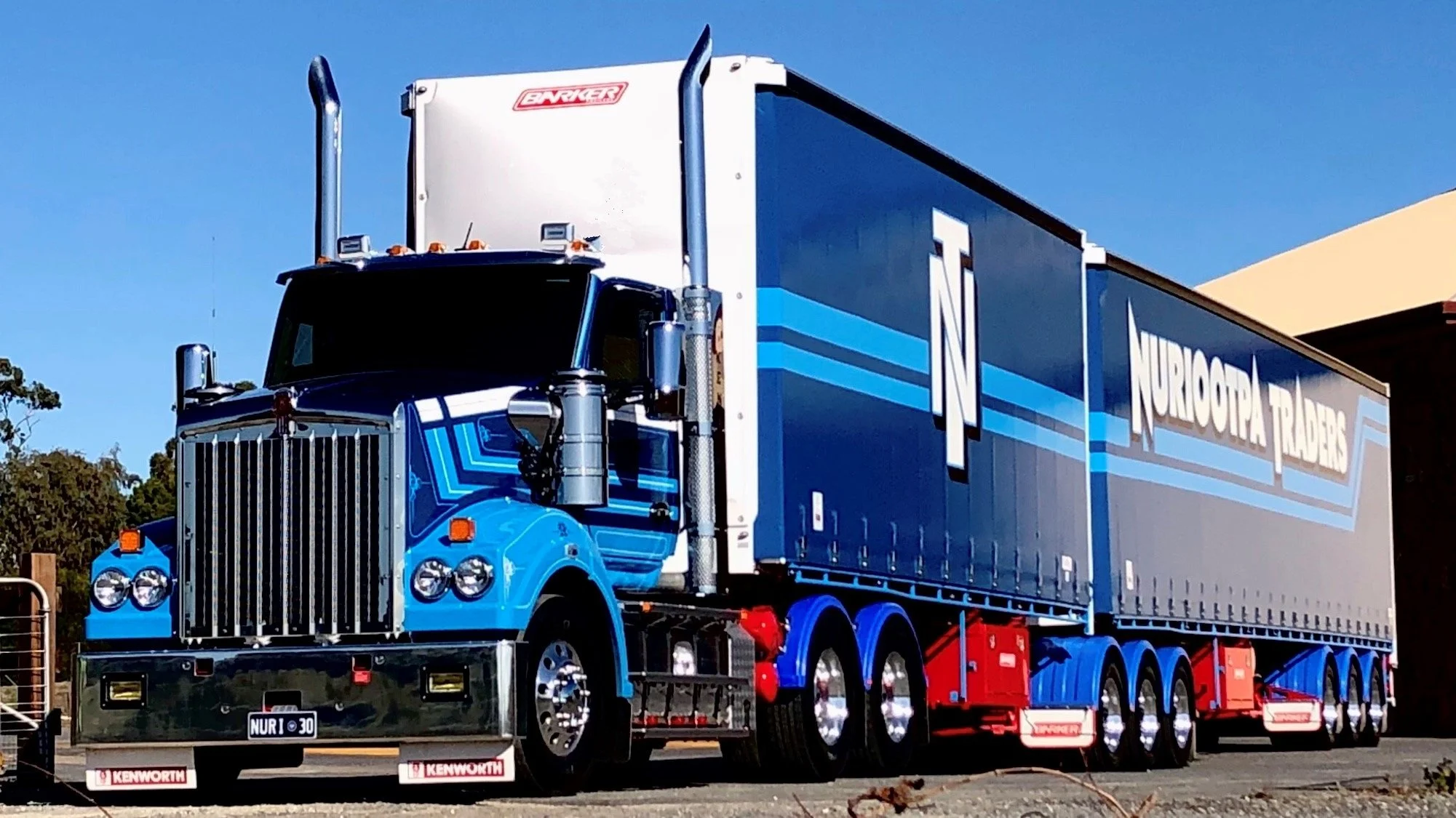 Blue semi-truck with 'Nuroopia Traders' branding parked outdoors against a clear blue sky, featuring detailed chrome accents and multiple wheels.