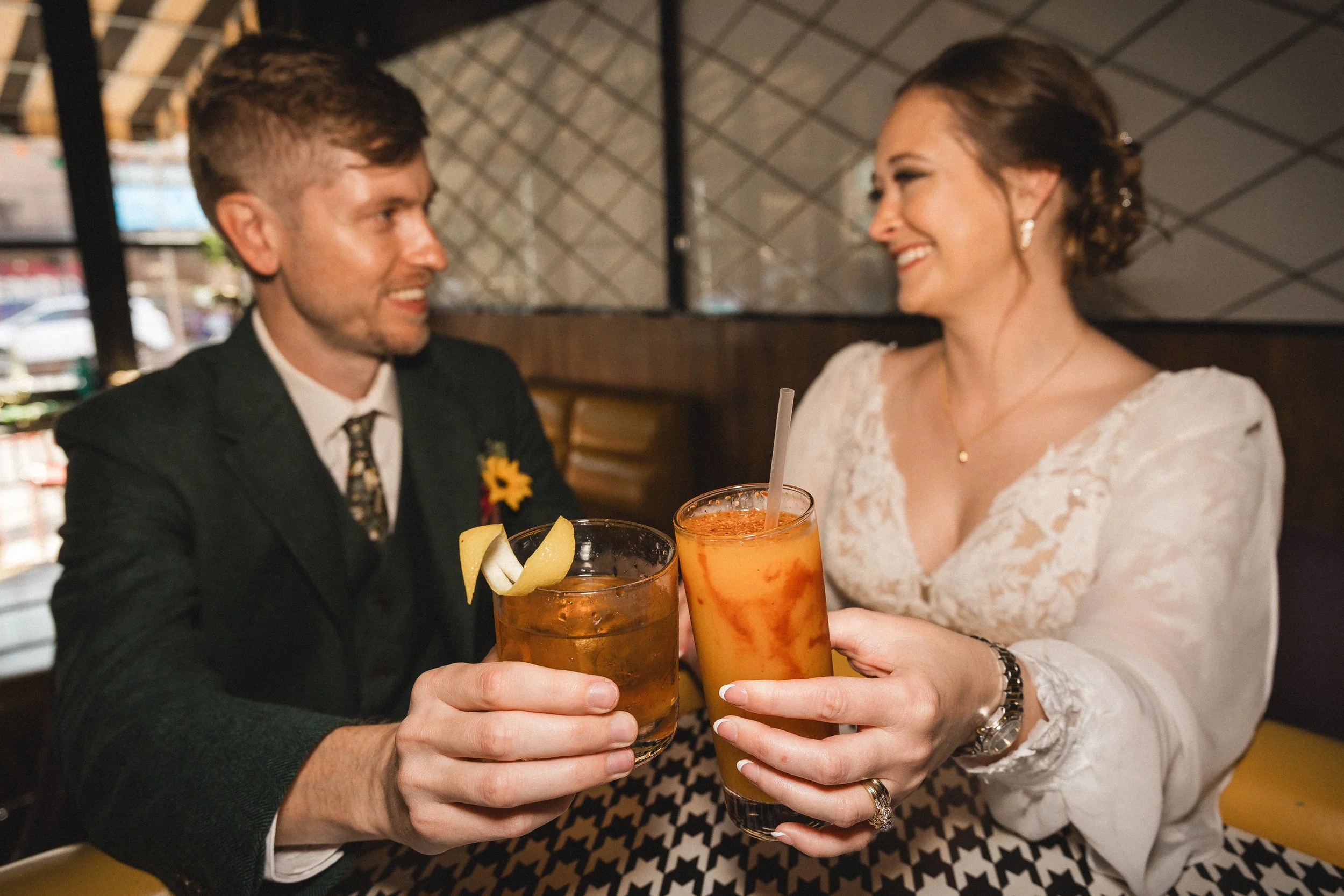 A couple dressed in semi-formal attire smiling and clinking glasses of drinks in a restaurant or bar.