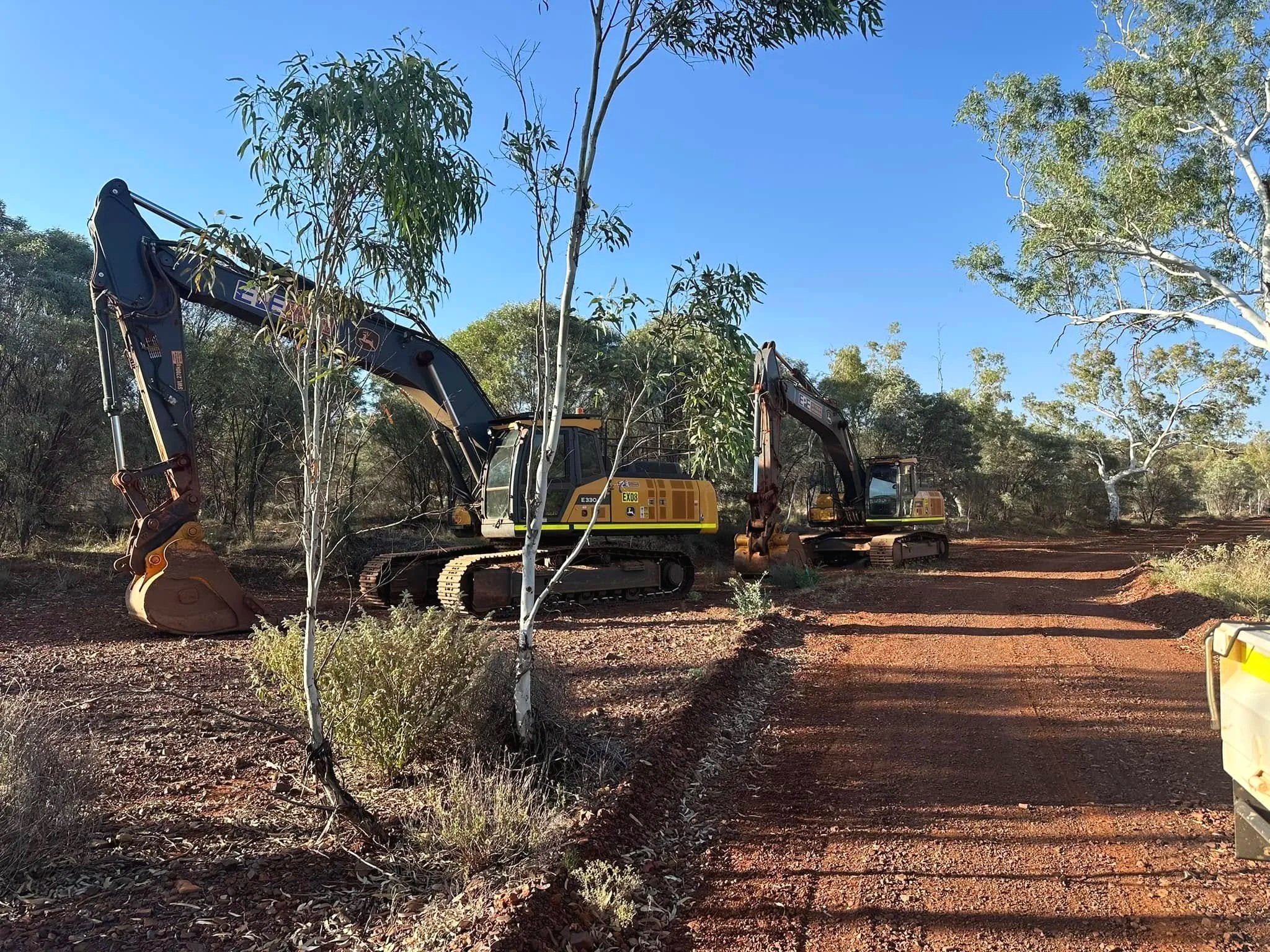 Construction excavators working on land with trees and clear blue sky background.