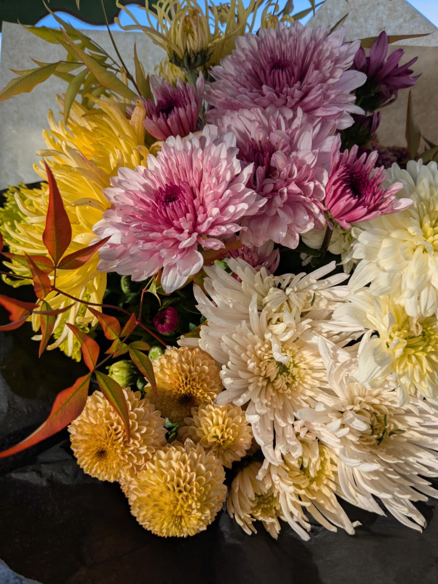 A colorful bouquet of various flowers including pink, yellow, white, and orange blooms with green leaves.