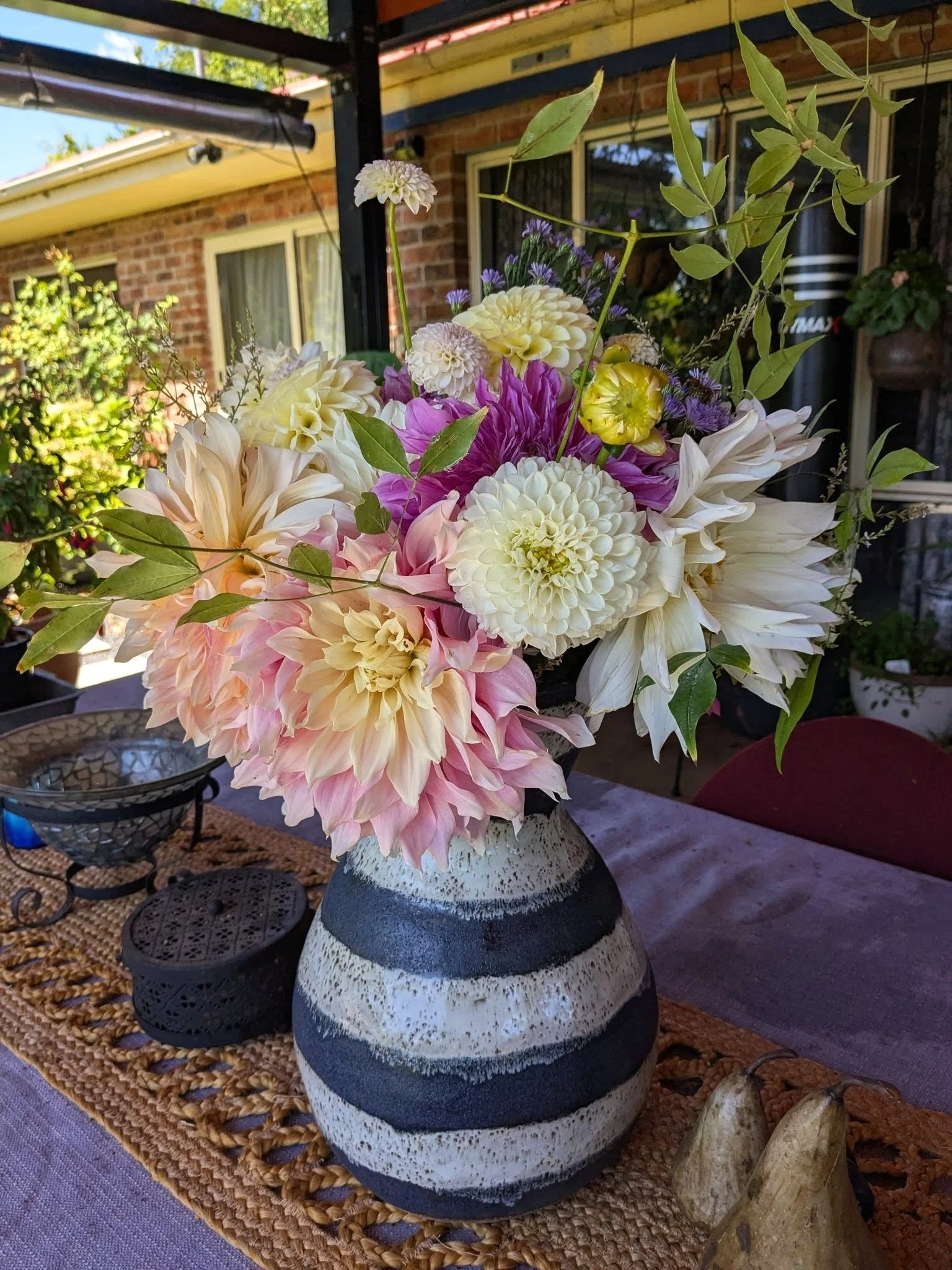 A bouquet of various colorful flowers in a striped ceramic vase on a table outdoors.