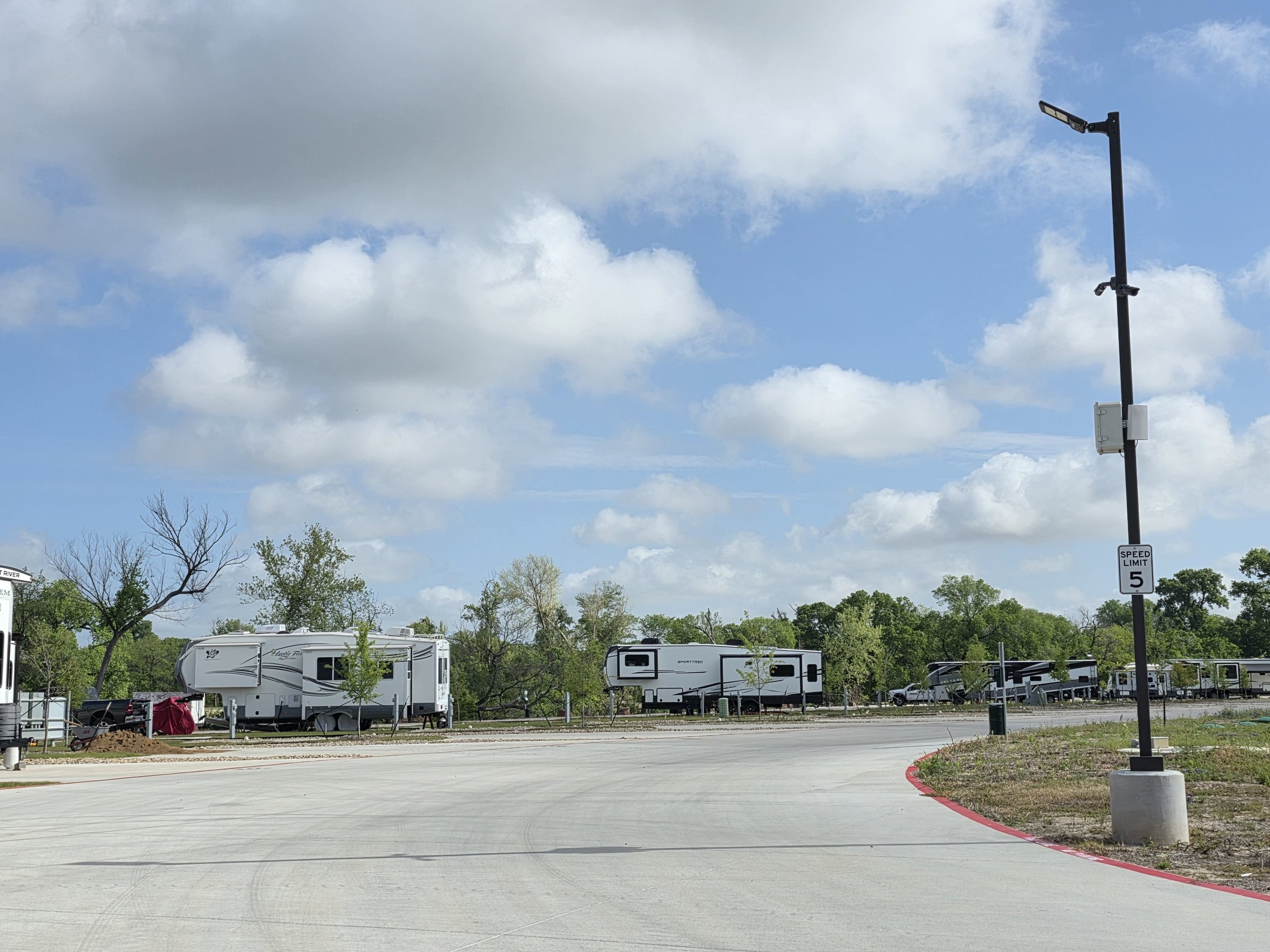 RVs on lots in the back of the RV Resort, post with speed limit sign and security cameras visible on right side of image.