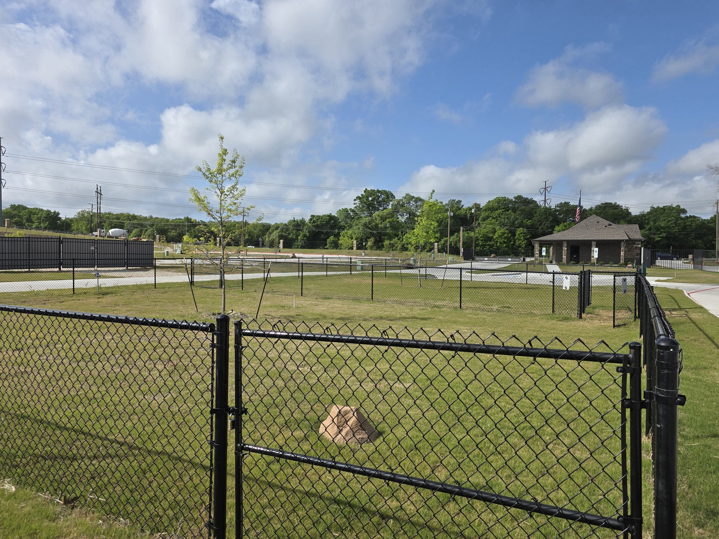 Dog park area with green grass and tree, fenced in.