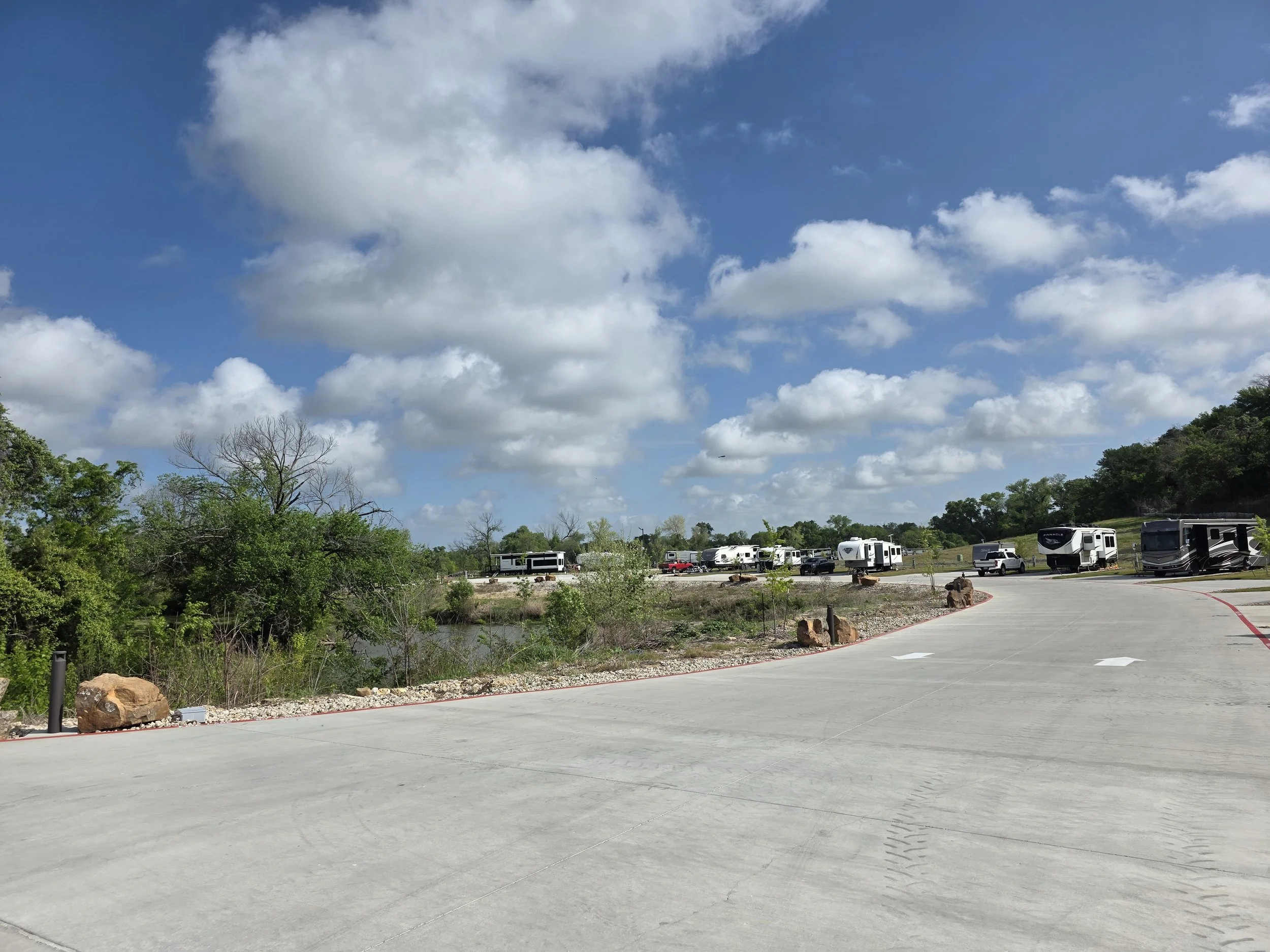 Sunny day looking down road that leads to back of RV park, RVs visible in the background, clouds in the sky.