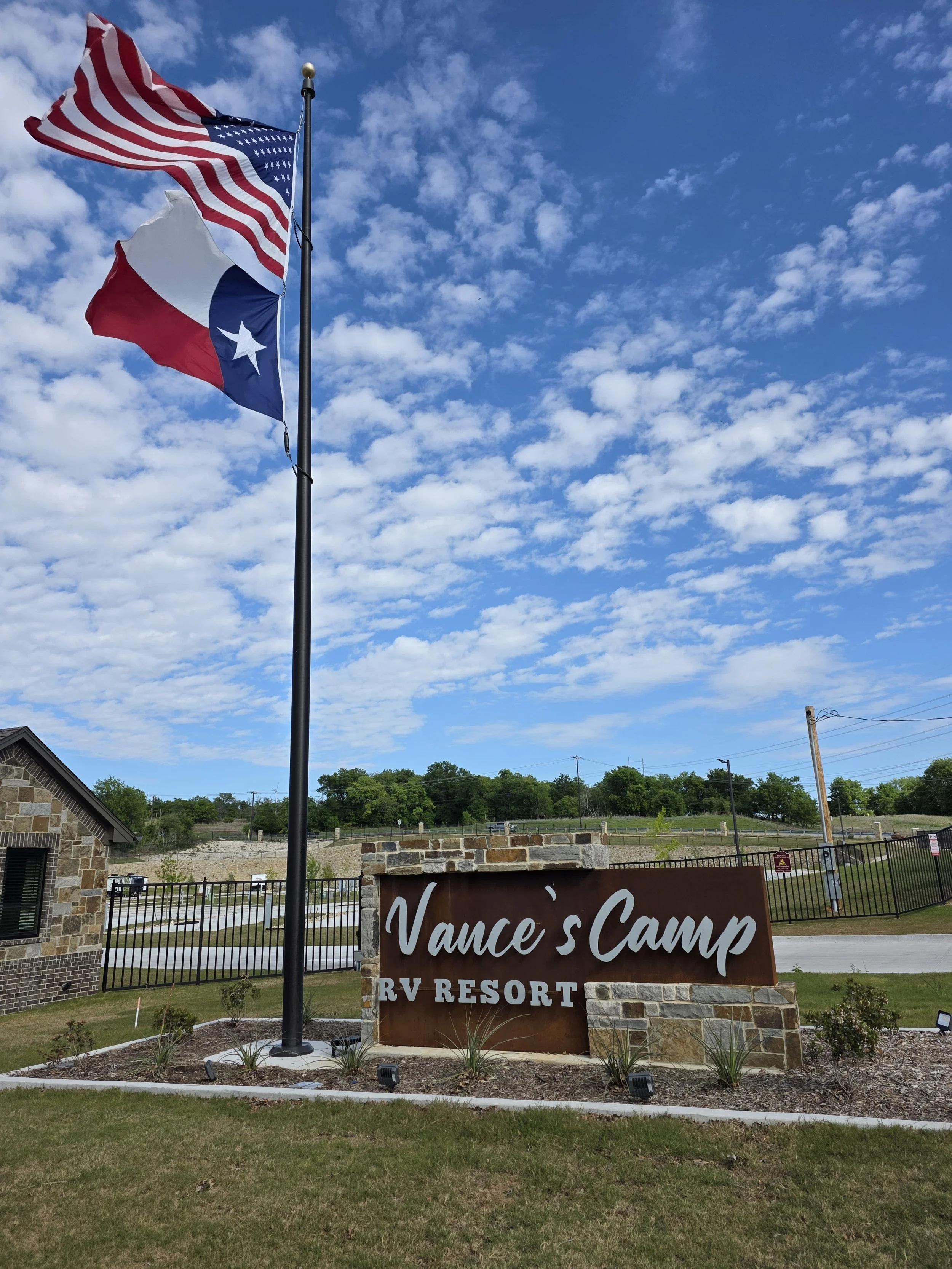 Sign that reads Vance's Camp RV resort, sunny day, American and Texas State flags waving in the wind