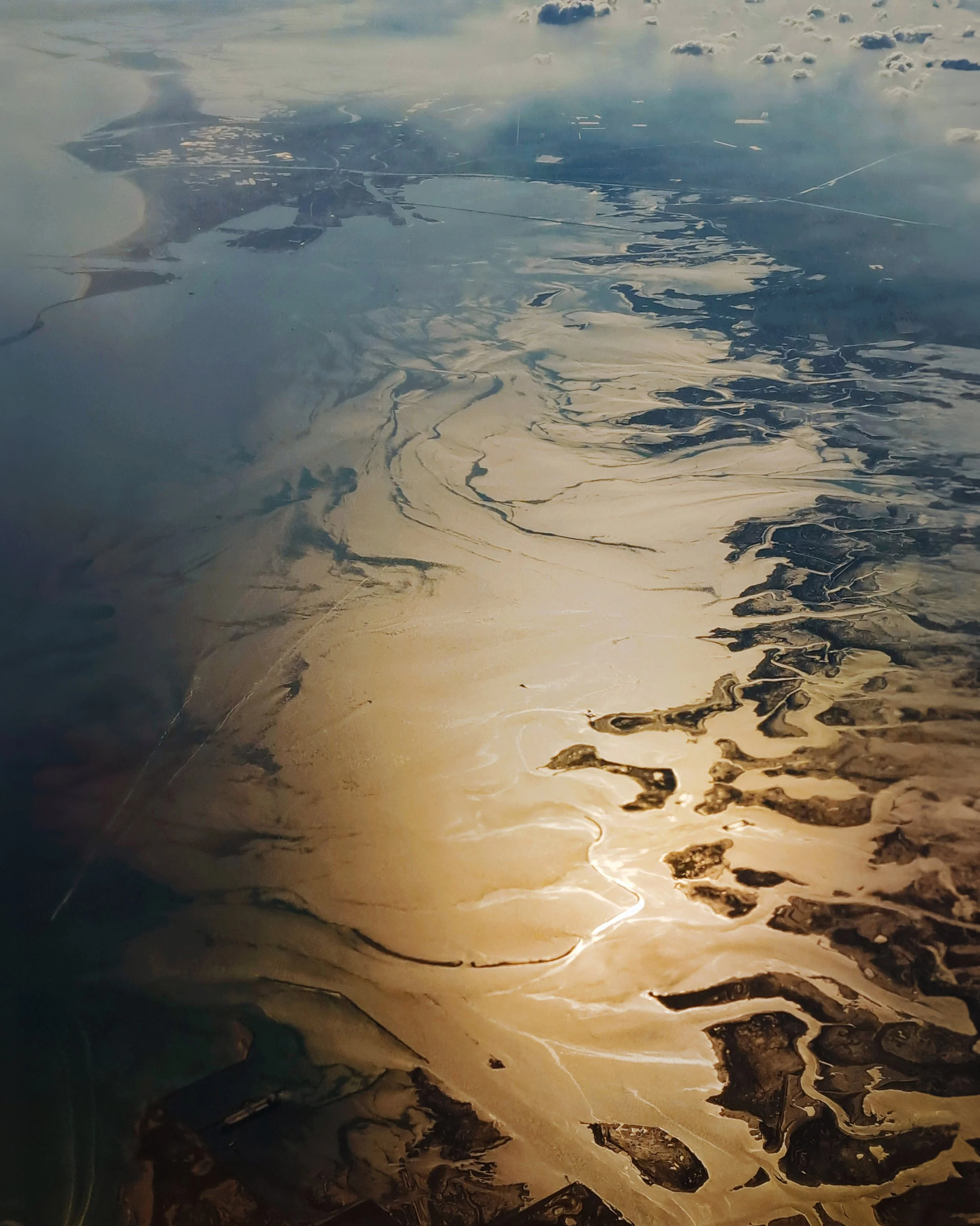Vista aerea di un paesaggio naturale con corsi d'acqua, sabbia e terreni aridi, riflessi dorati del sole.