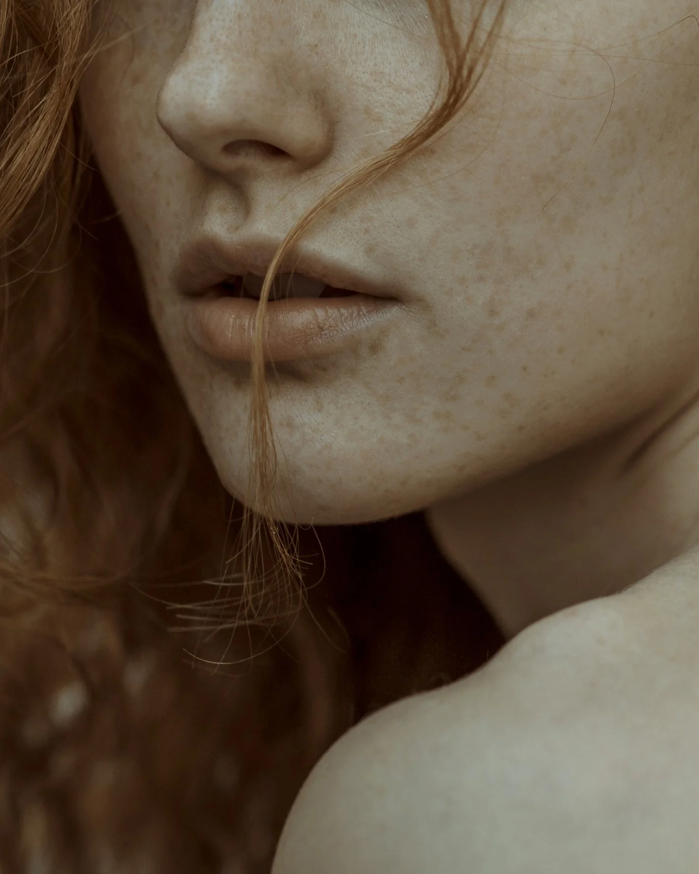 Dettaglio ravvicinato di un volto di donna, con pelle chiara, lentiggini e capelli rossi, inquadratura sul naso, labbra e parte della guancia.