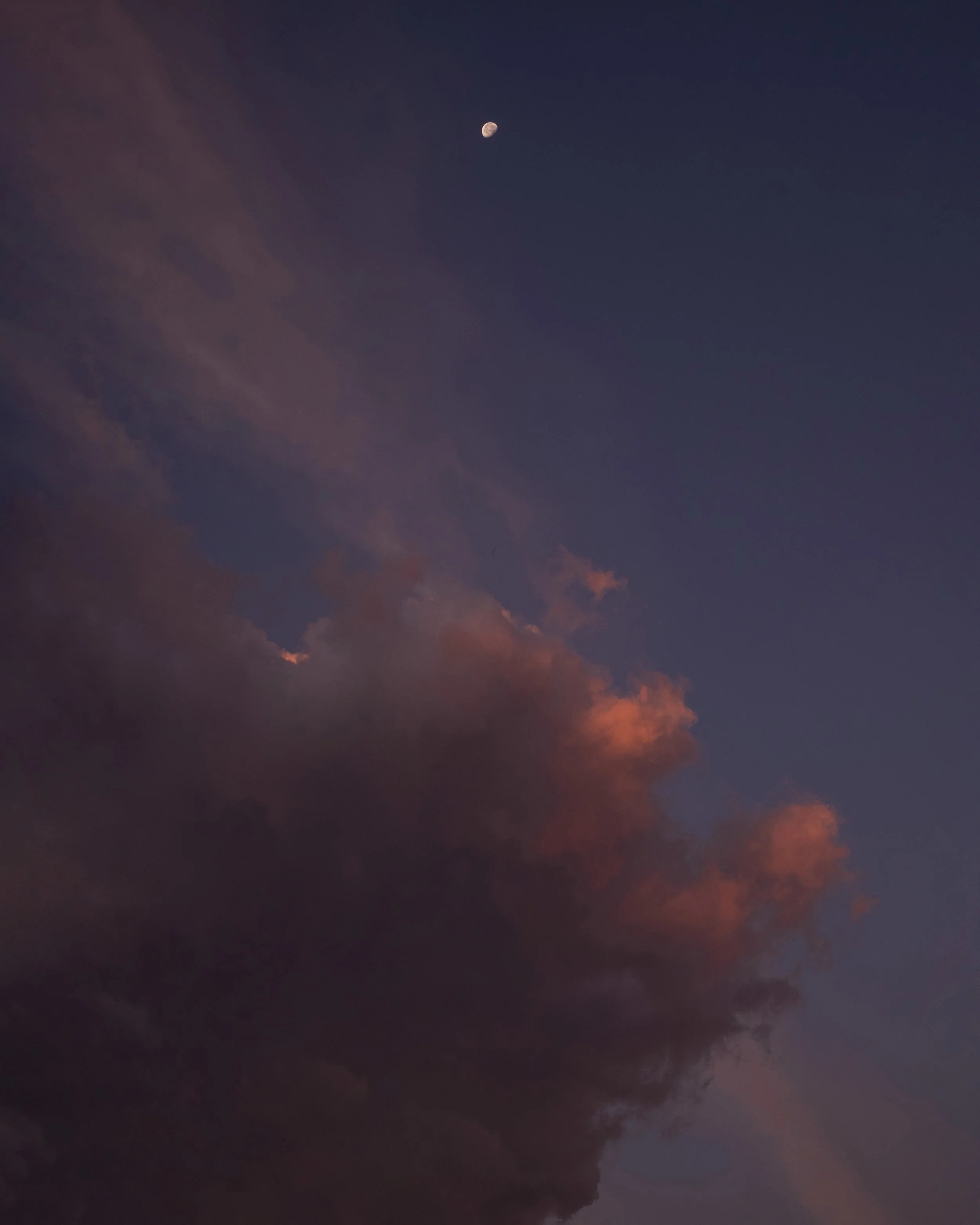 Cielo al tramonto con nuvole rosa e arancioni e la luna visibile in alto a sinistra.