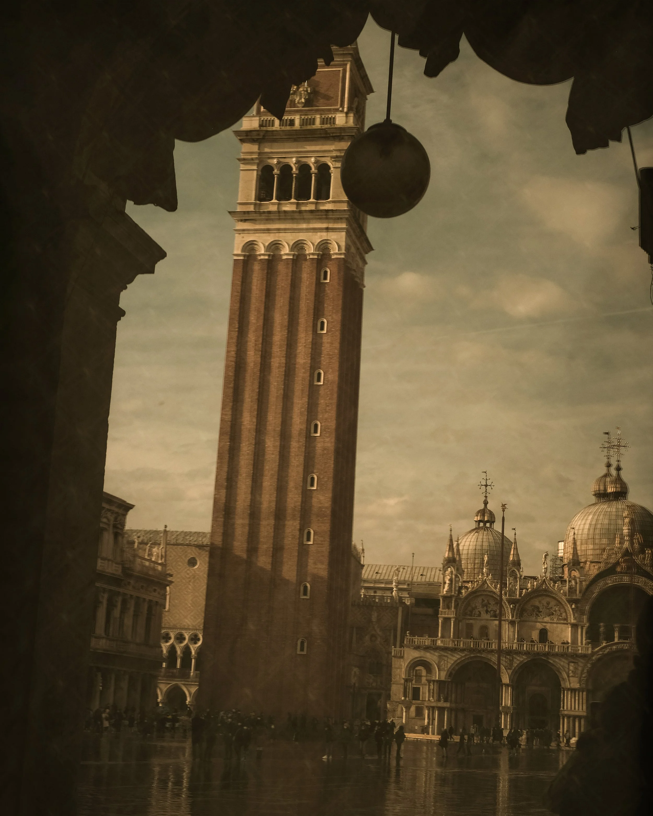 Vista di Piazza San Marco a Venezia con il campanile e la basilica, incorniciata da archi e tessiture di ombre e luci.