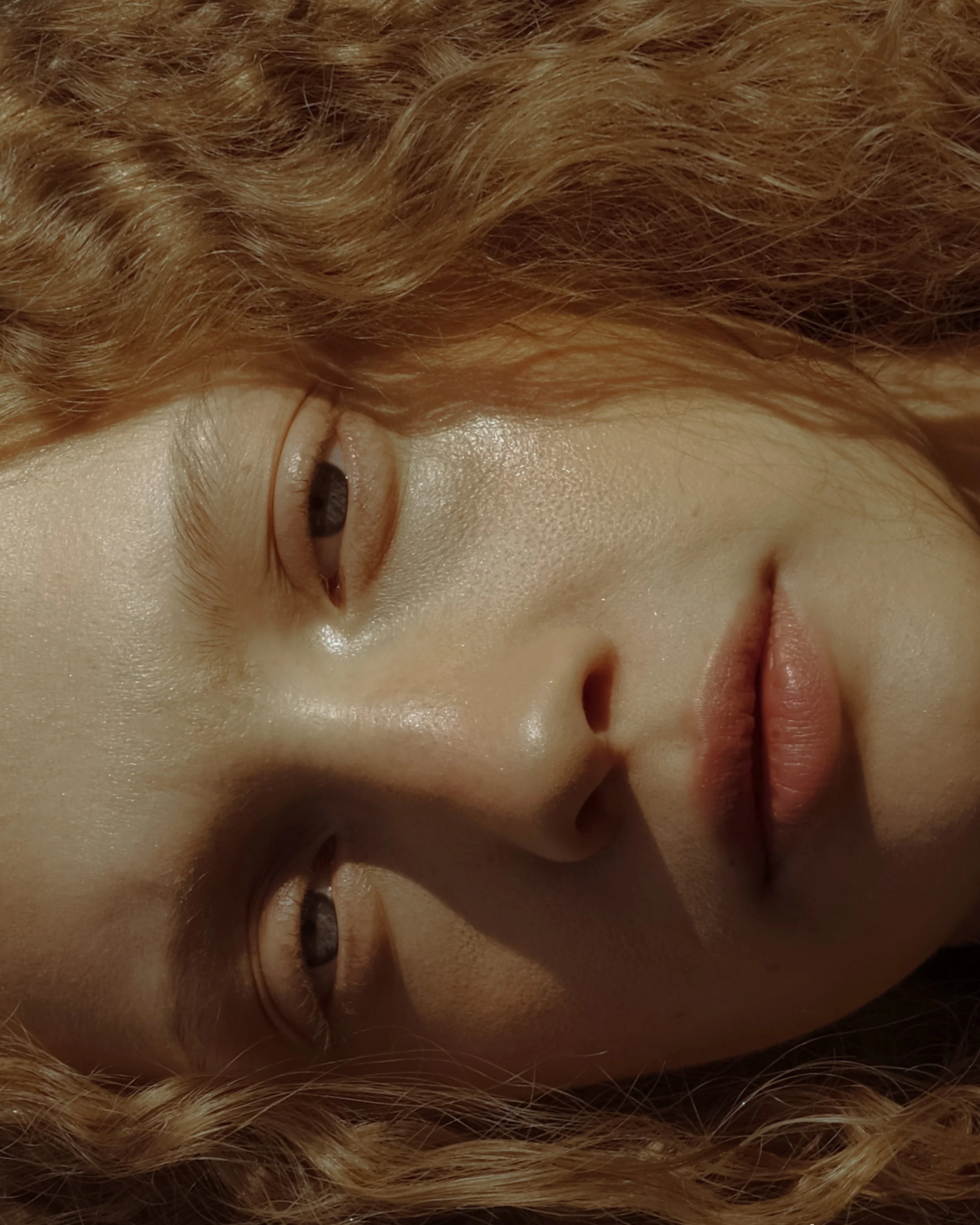 Primo piano di un volto di donna con capelli ricci biondi e pelle luminosa.