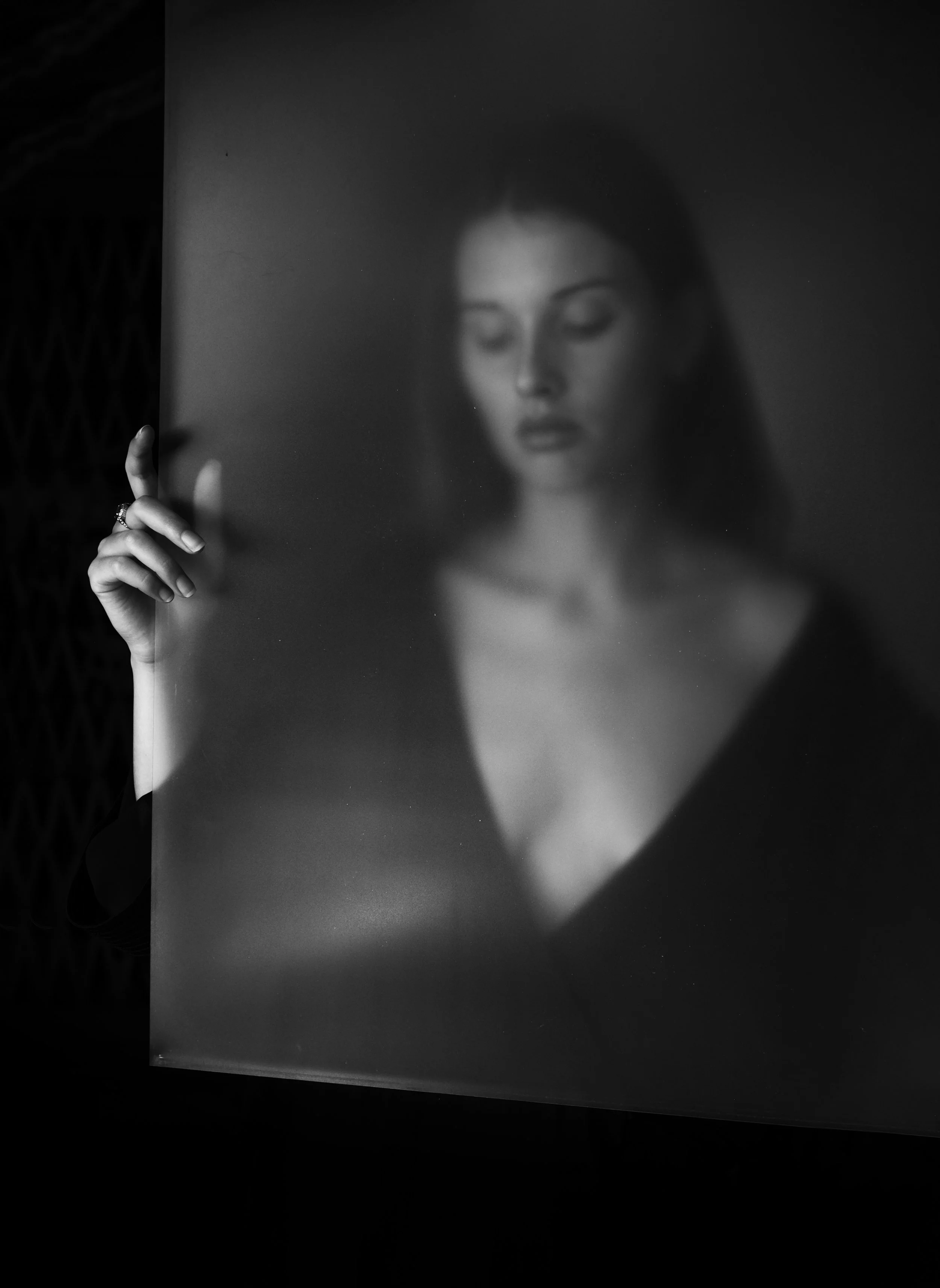 Donna dietro un vetro smerigliato, in bianco e nero, tocca il vetro con una mano, volto sfocato.