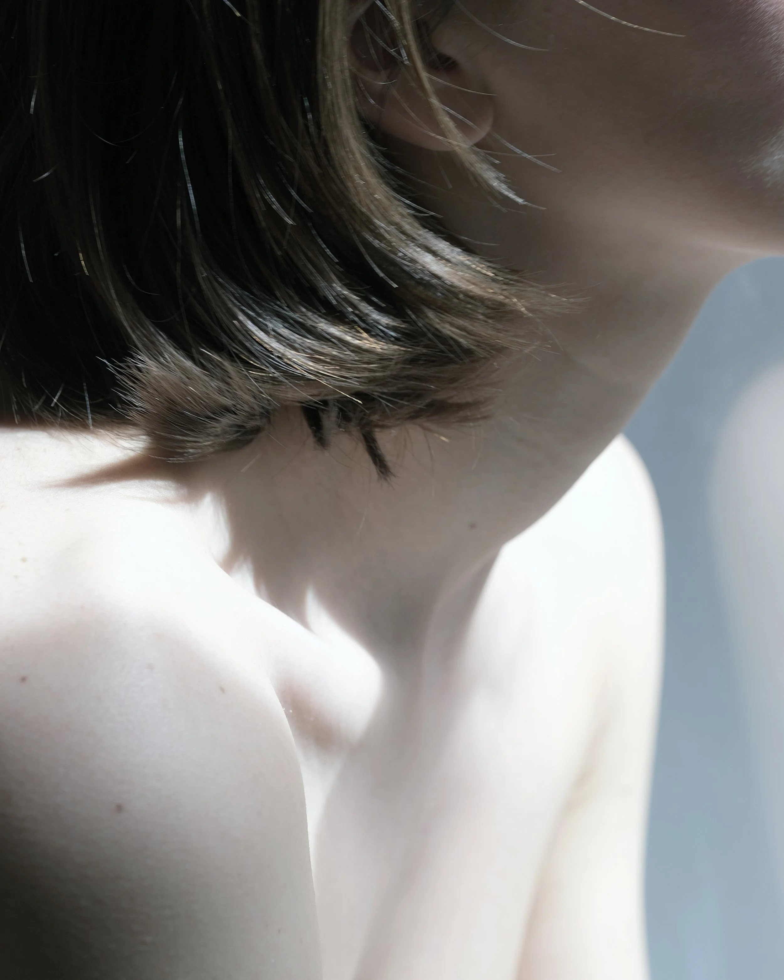 Primo piano di una persona con capelli castani e pelle chiara, vista dal lato. La fotografia mette in risalto il collo e la spalla.