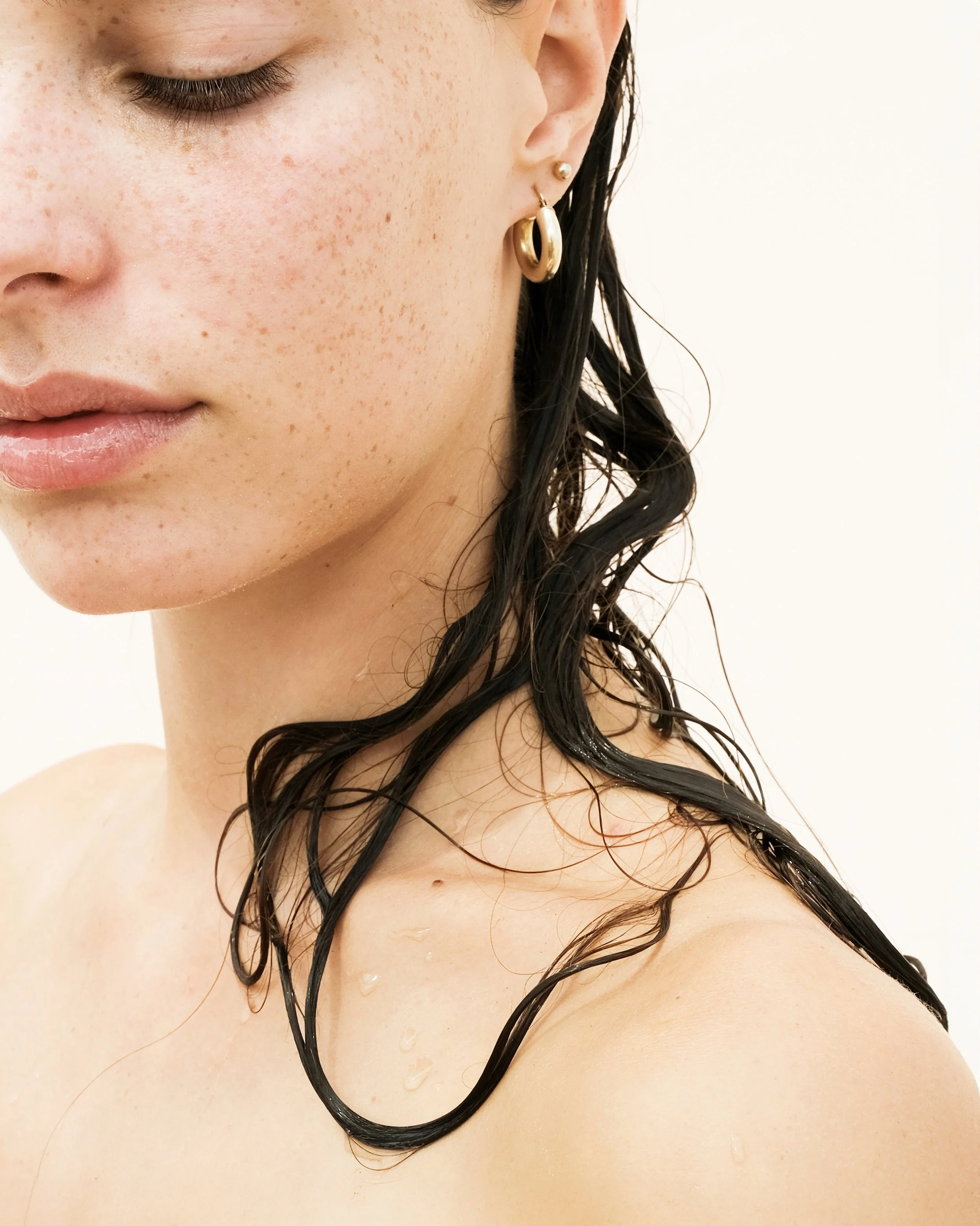 Primo piano di una donna con capelli bagnati e orecchini in oro.
