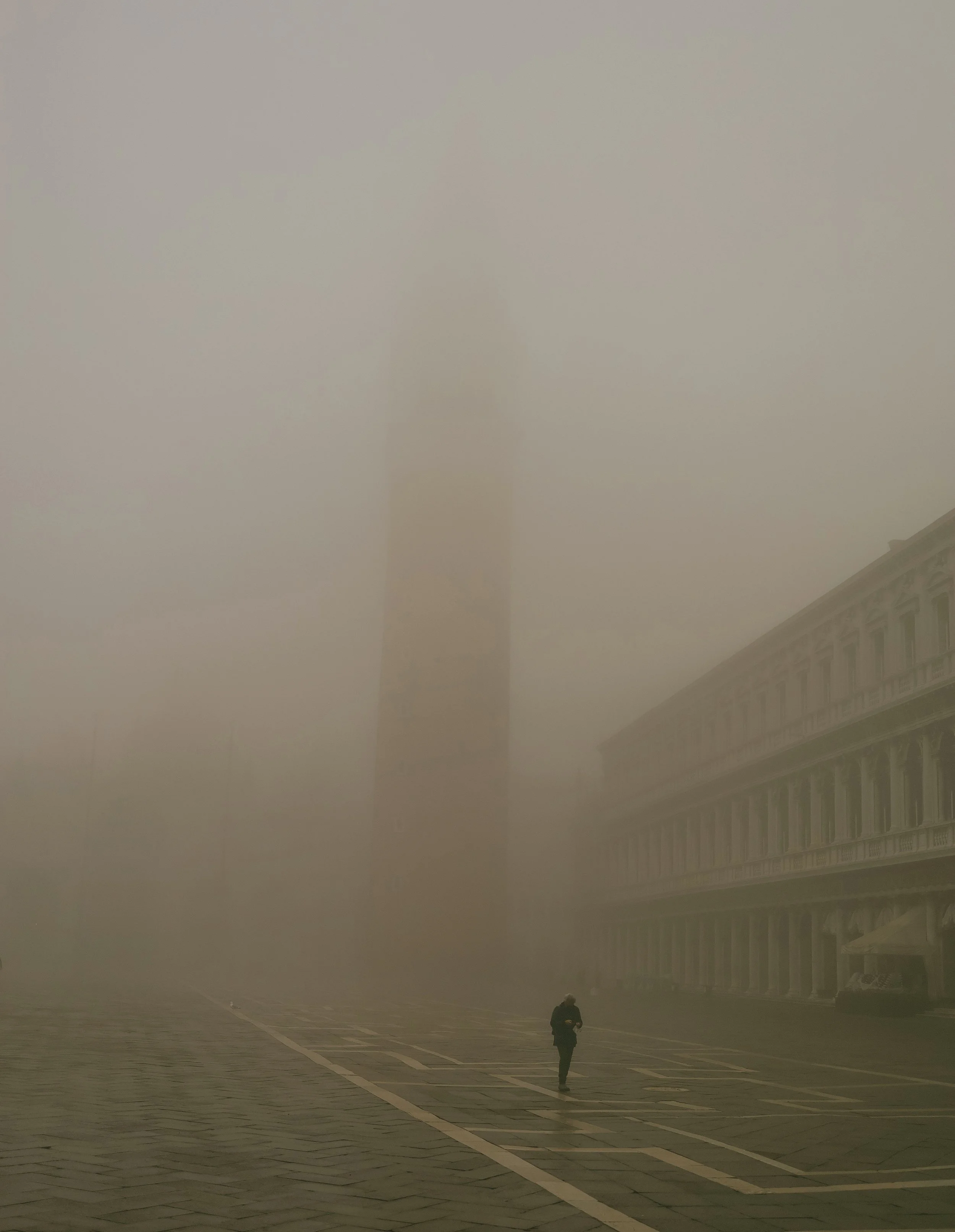Una persona cammina in una Piazza di Venezia avvolta dalla nebbia, con il Colosseo visibile in lontananza