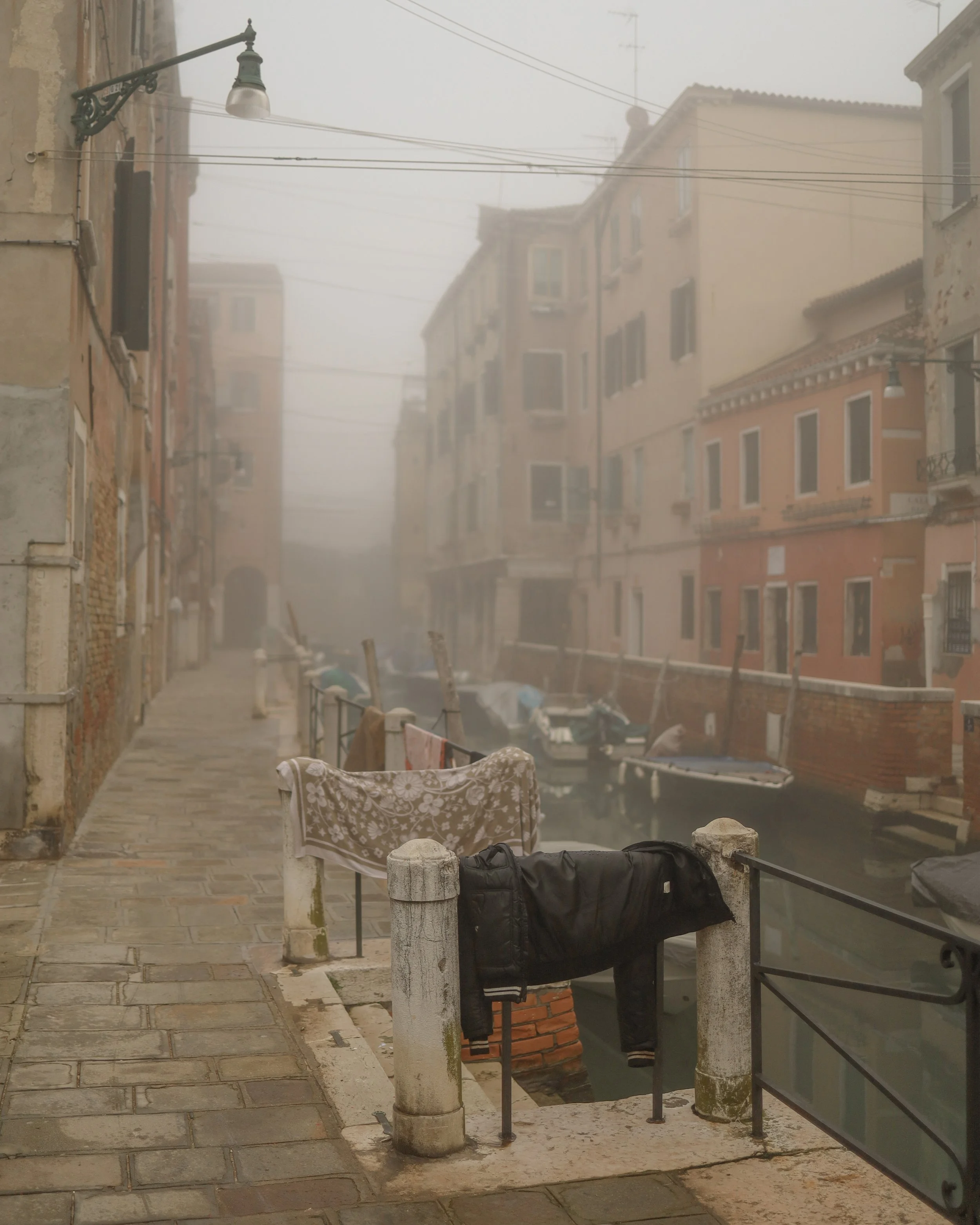 Una scena di una calle di Venezia con edifichi colorati, gondole ormeggiate in un canale e una nebbia fitta che riduce la visibilità.