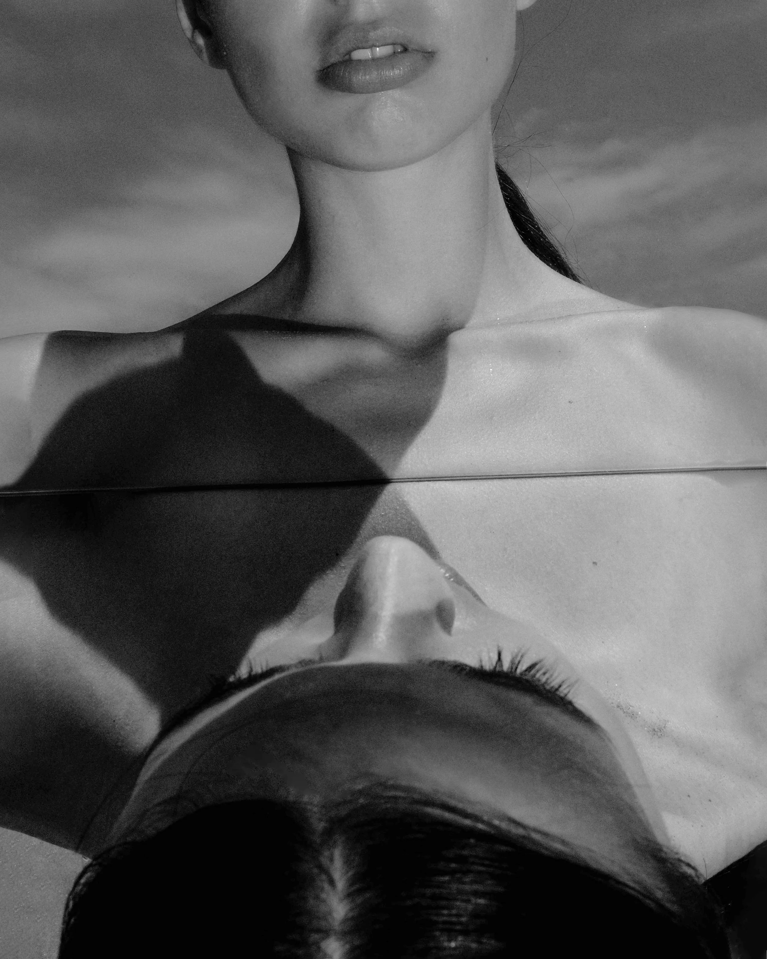 Primo piano di una parte del viso e del collo di una donna riflessa in uno specchio, in un'immagine in bianco e nero.